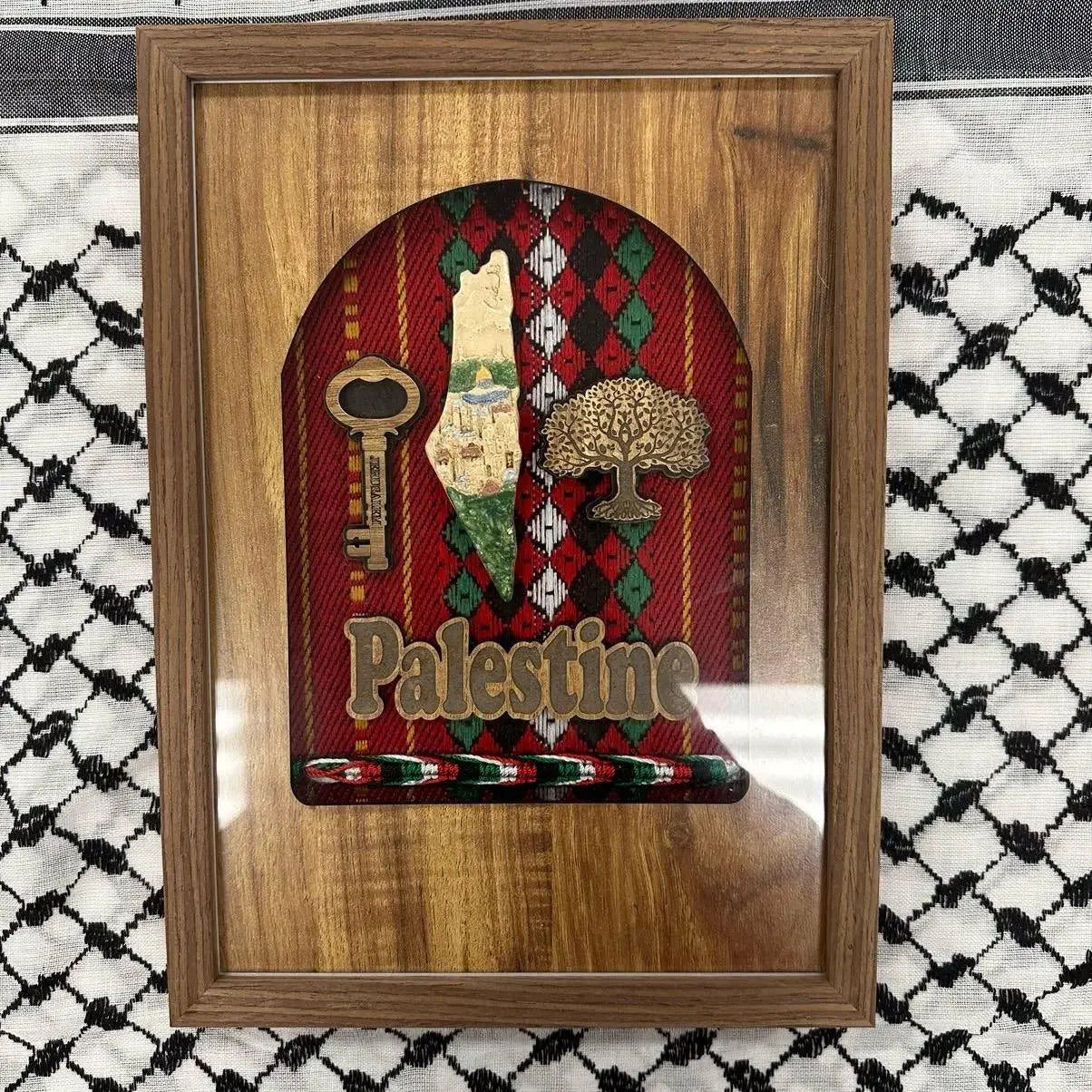 Palestinian embroidered wall art with wooden frame featuring map, key, tree, and Palestine text on red patterned fabric