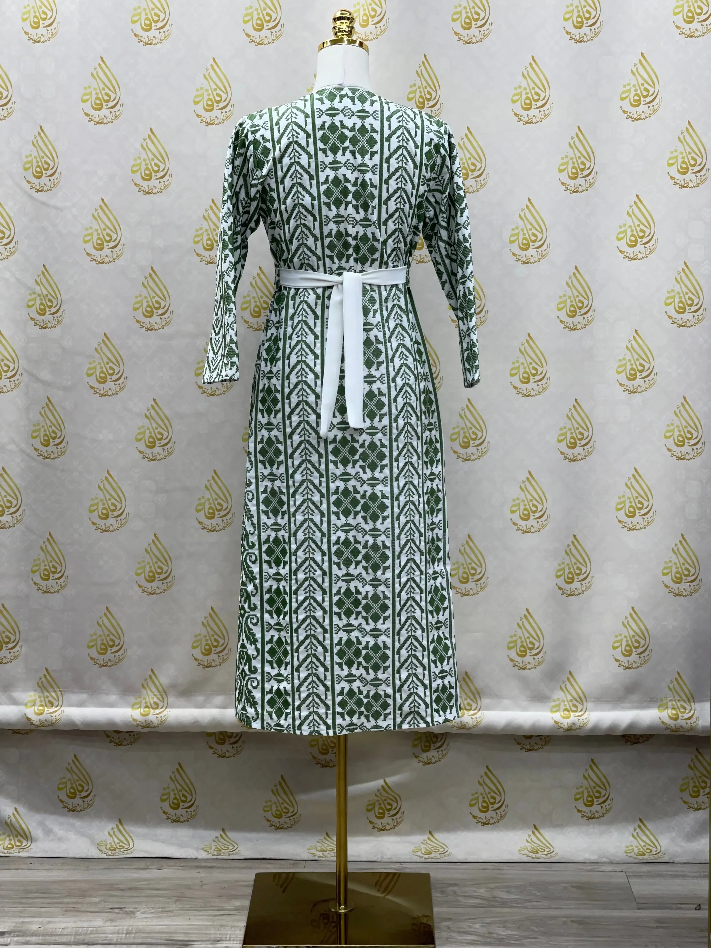 Palestinian Elegance embroidered cardigan for kids with green geometric patterns and white belt on a mannequin