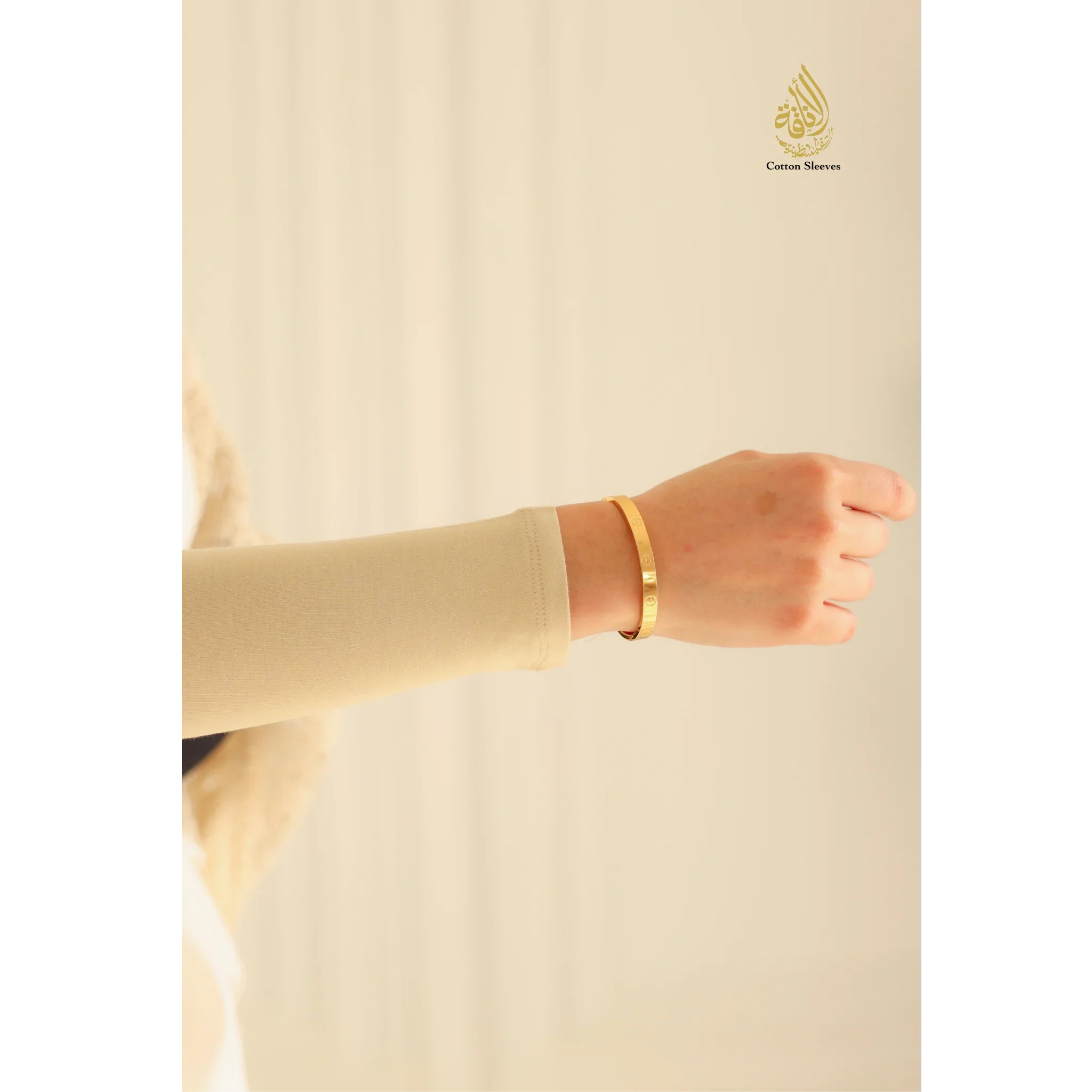 Gold bracelet on a hand against a beige background with a brand logo.