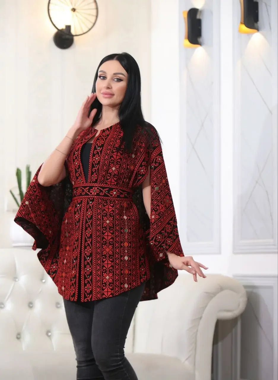 Woman wearing Palestinian Elegance embroidered cape jacket with red and black traditional patterns indoors