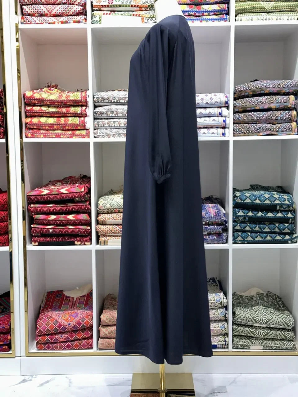 Palestinian Elegance black umra abaya for women displayed on mannequin in front of colorful fabric shelves