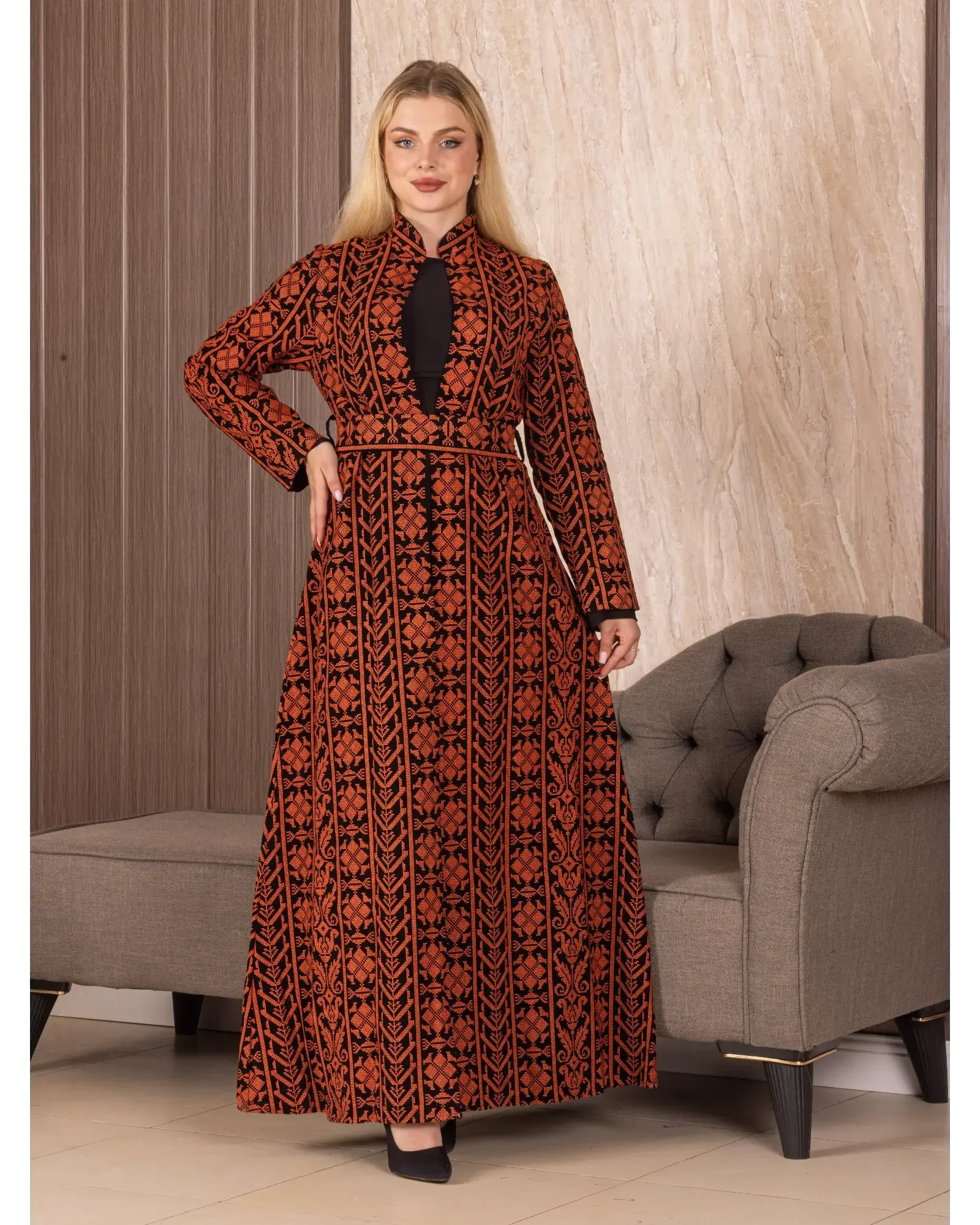 Woman wearing a Palestinian Elegance embroidered long cardigan with red and black intricate patterns standing indoors