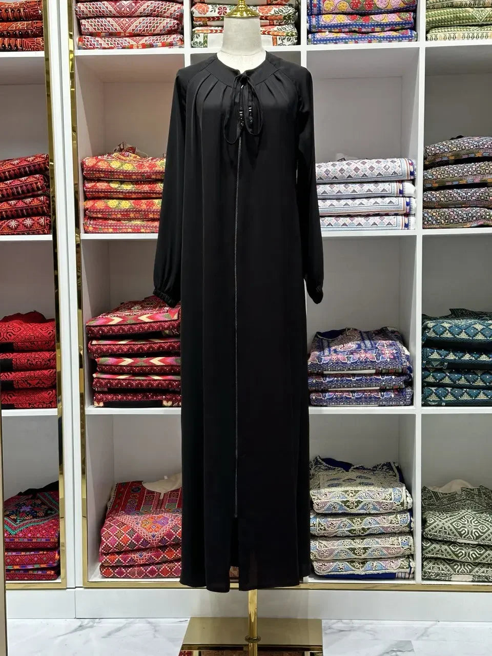 Palestinian Elegance black umra abaya for women displayed on mannequin in front of colorful traditional fabric shelves