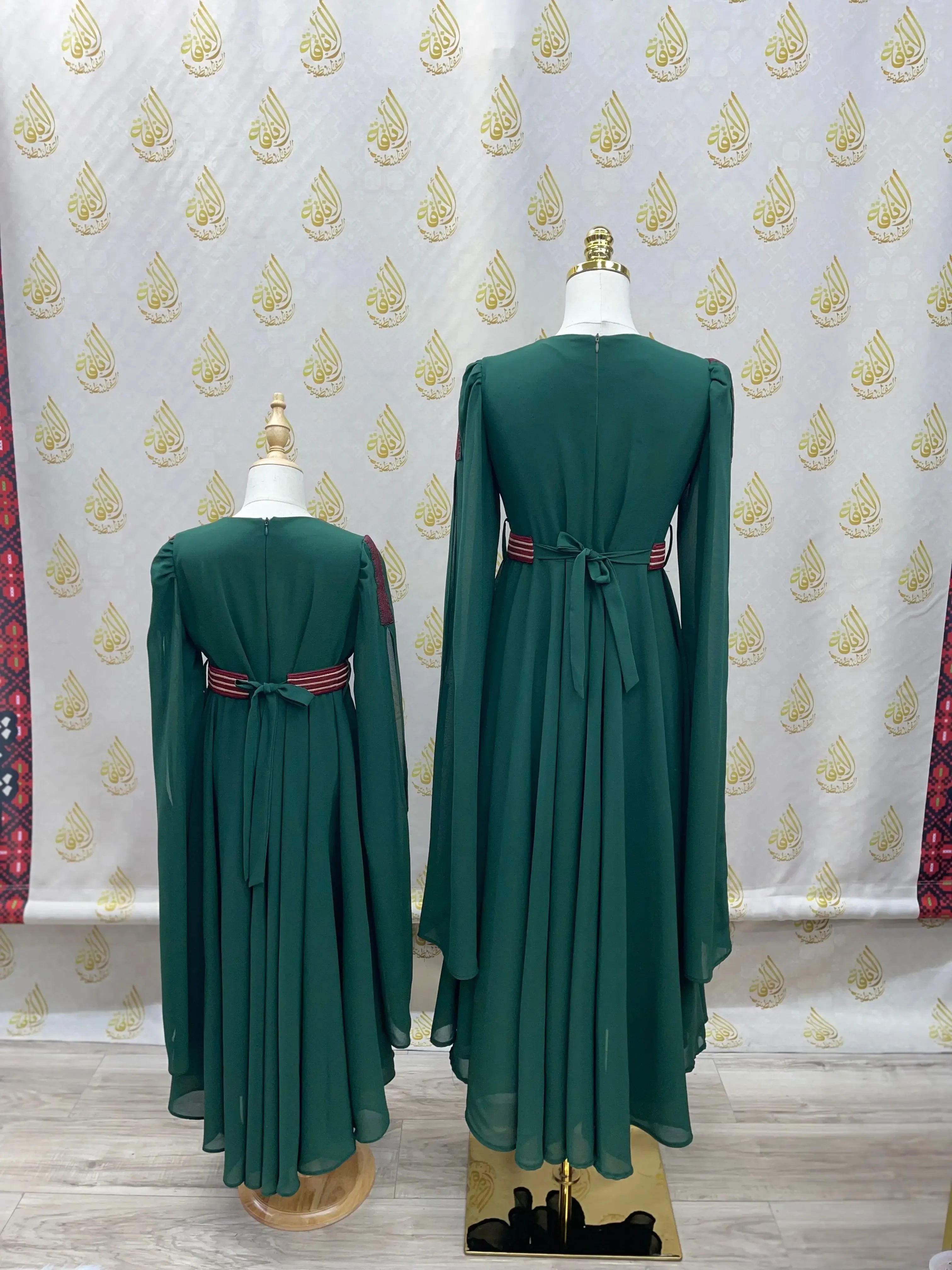 Palestinian girls embroidered dress in green with long sleeves and a tied waist belt displayed on mannequins