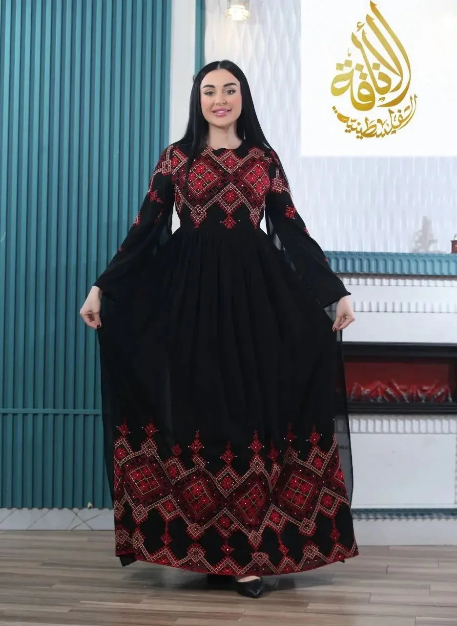 Black modern embroidered Palestinian dress with red geometric patterns worn by woman indoors