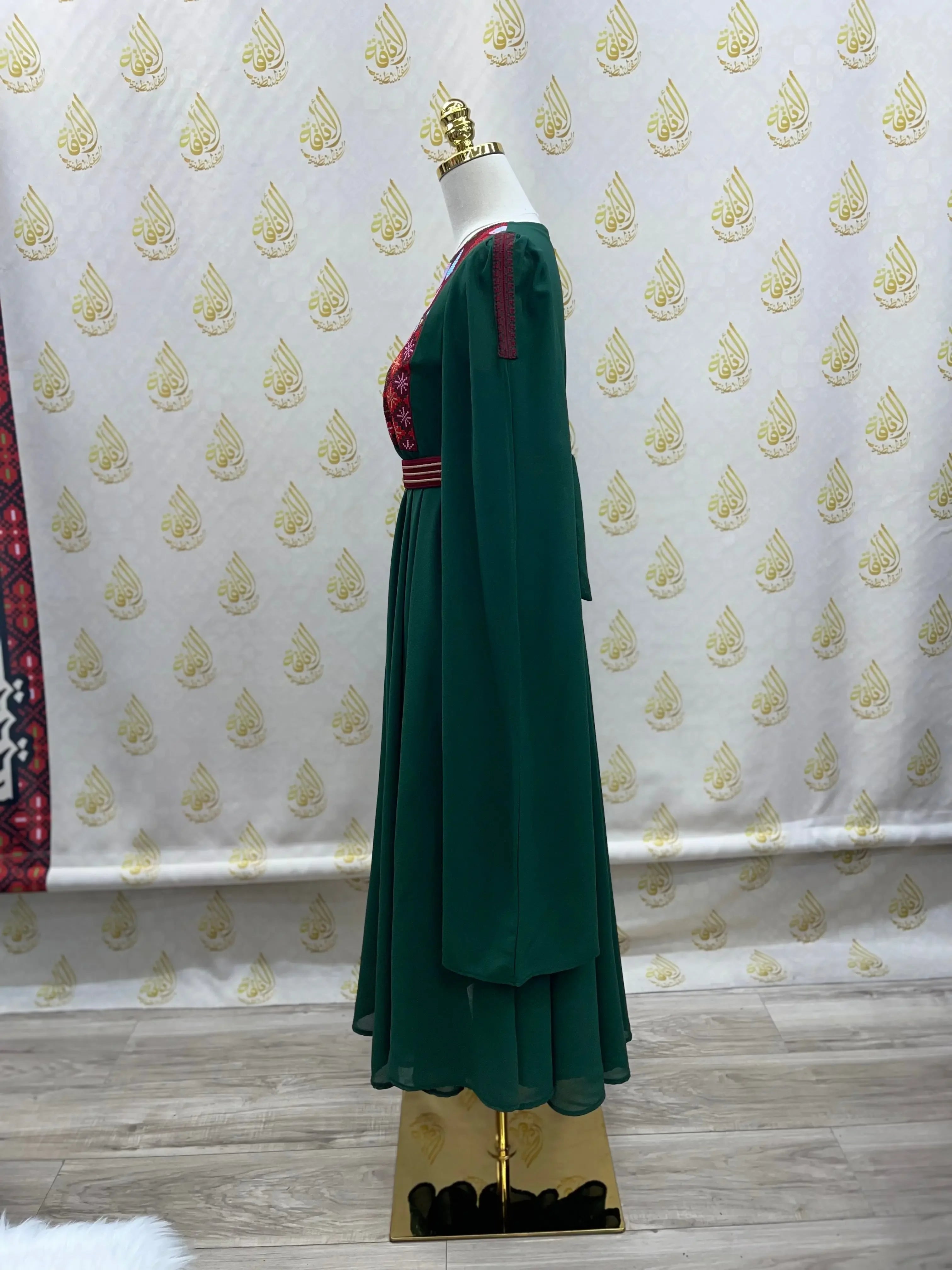Palestinian girls embroidered dress in green with red detailed embroidery and long sleeves on a mannequin
