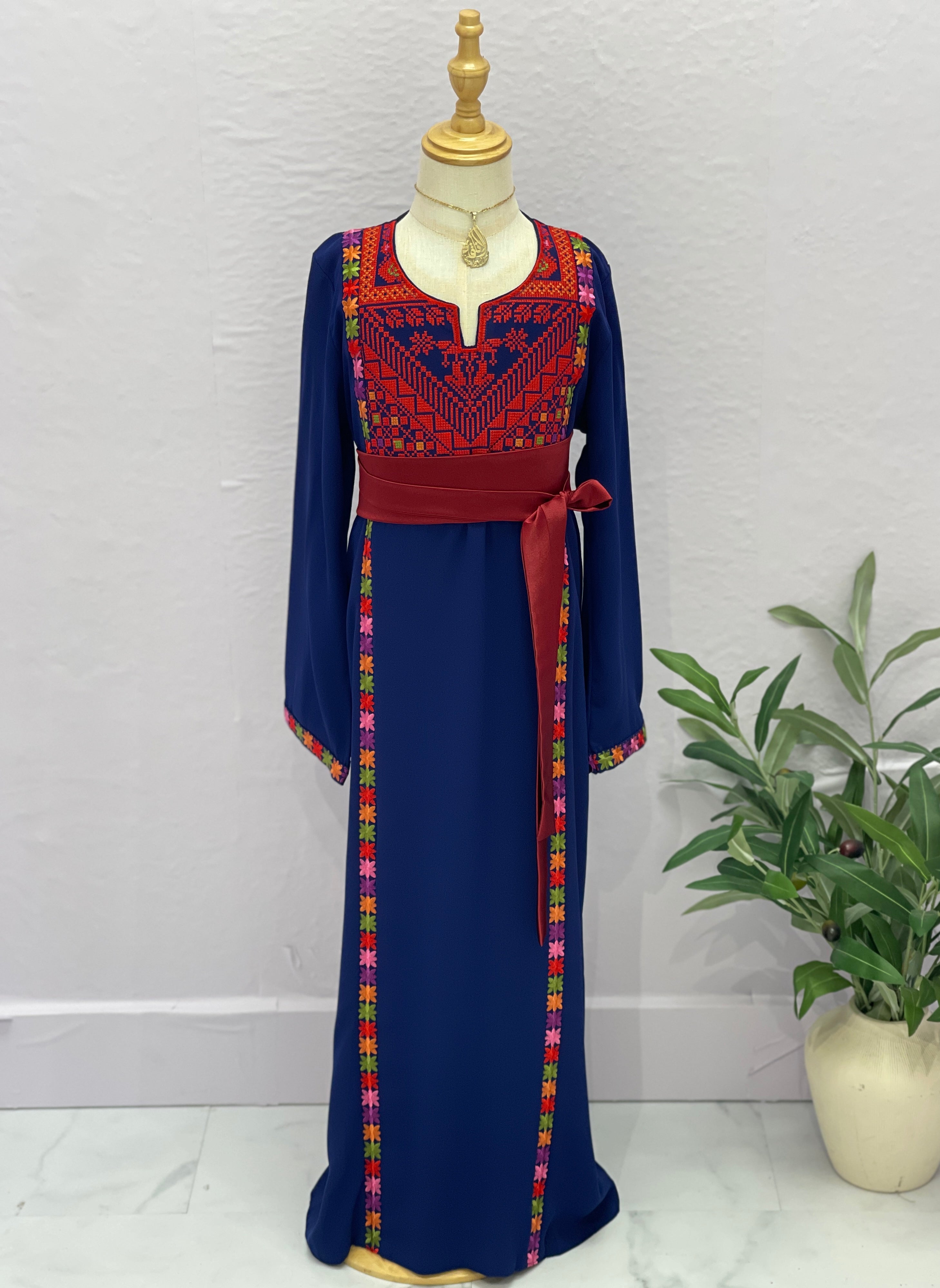 Traditional embroidered dress on a mannequin with a plant in the background