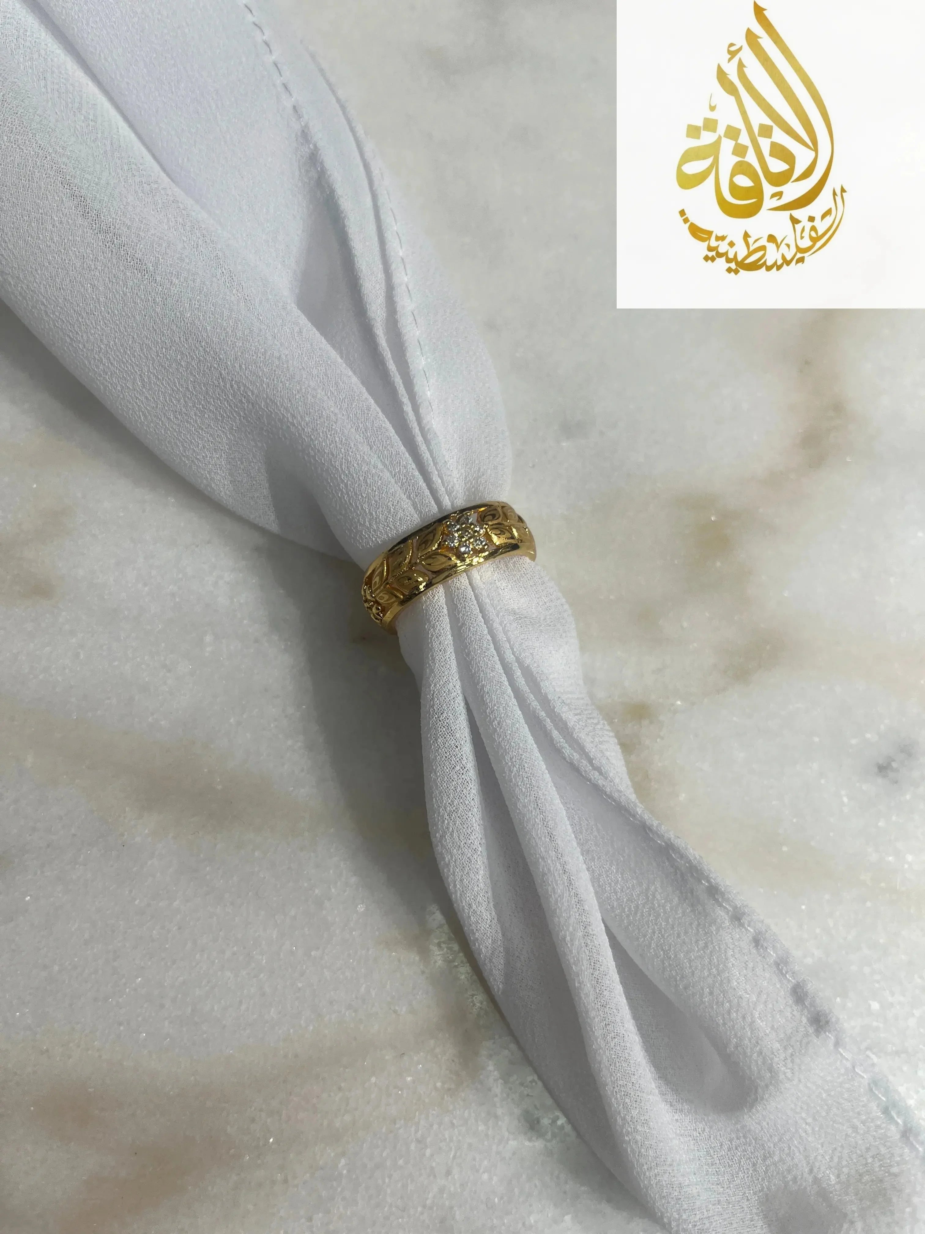 Floral gold imitation ring by Palestinian Elegance displayed on white cloth against marble background