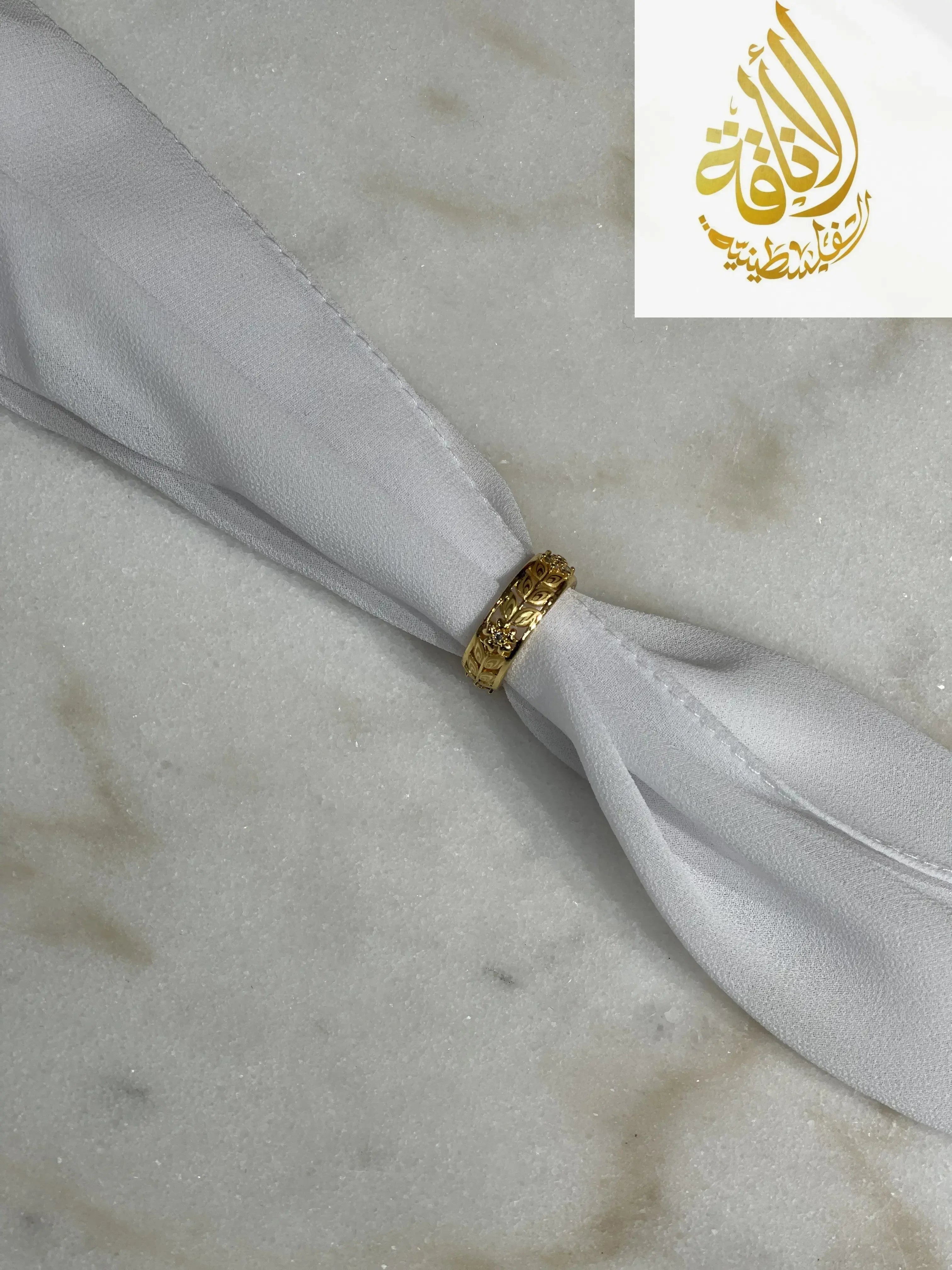 Floral gold imitation ring by Palestinian Elegance displayed on white fabric over marble surface