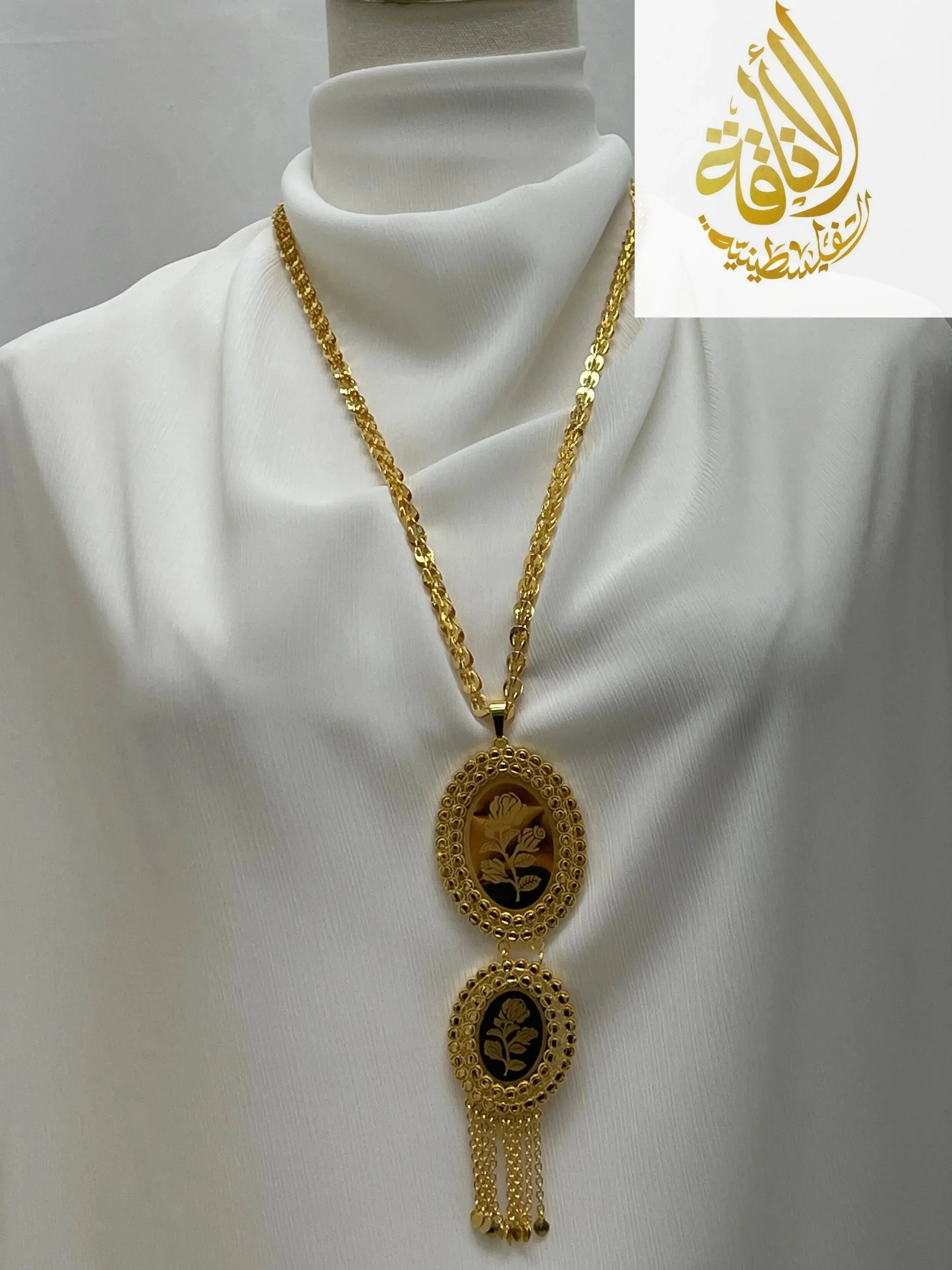 Palestinian Elegance imitated gold oval necklace with floral design and hanging chains on white fabric