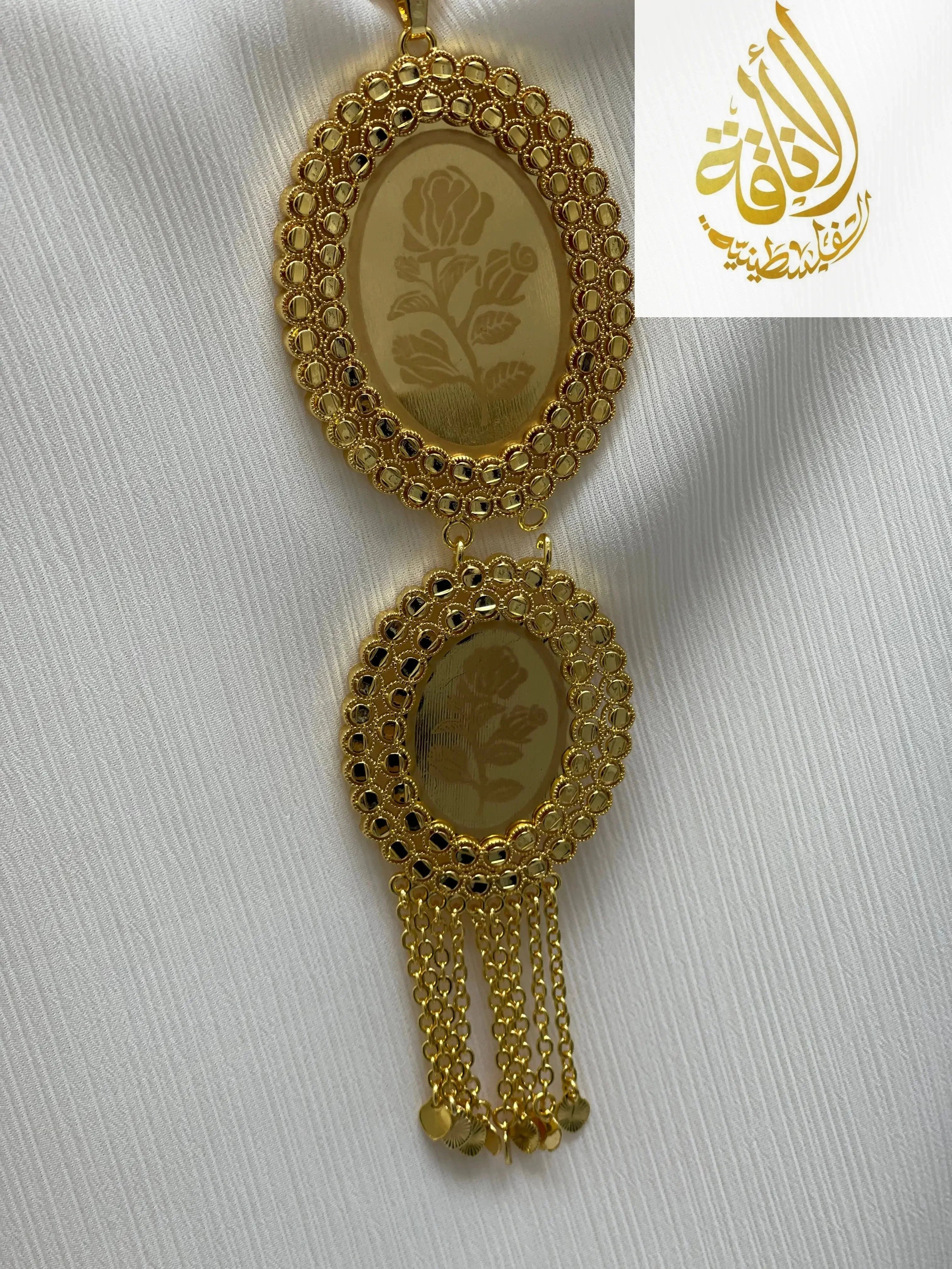 Palestinian Elegance imitated gold oval necklace with floral design and chain tassels on white fabric