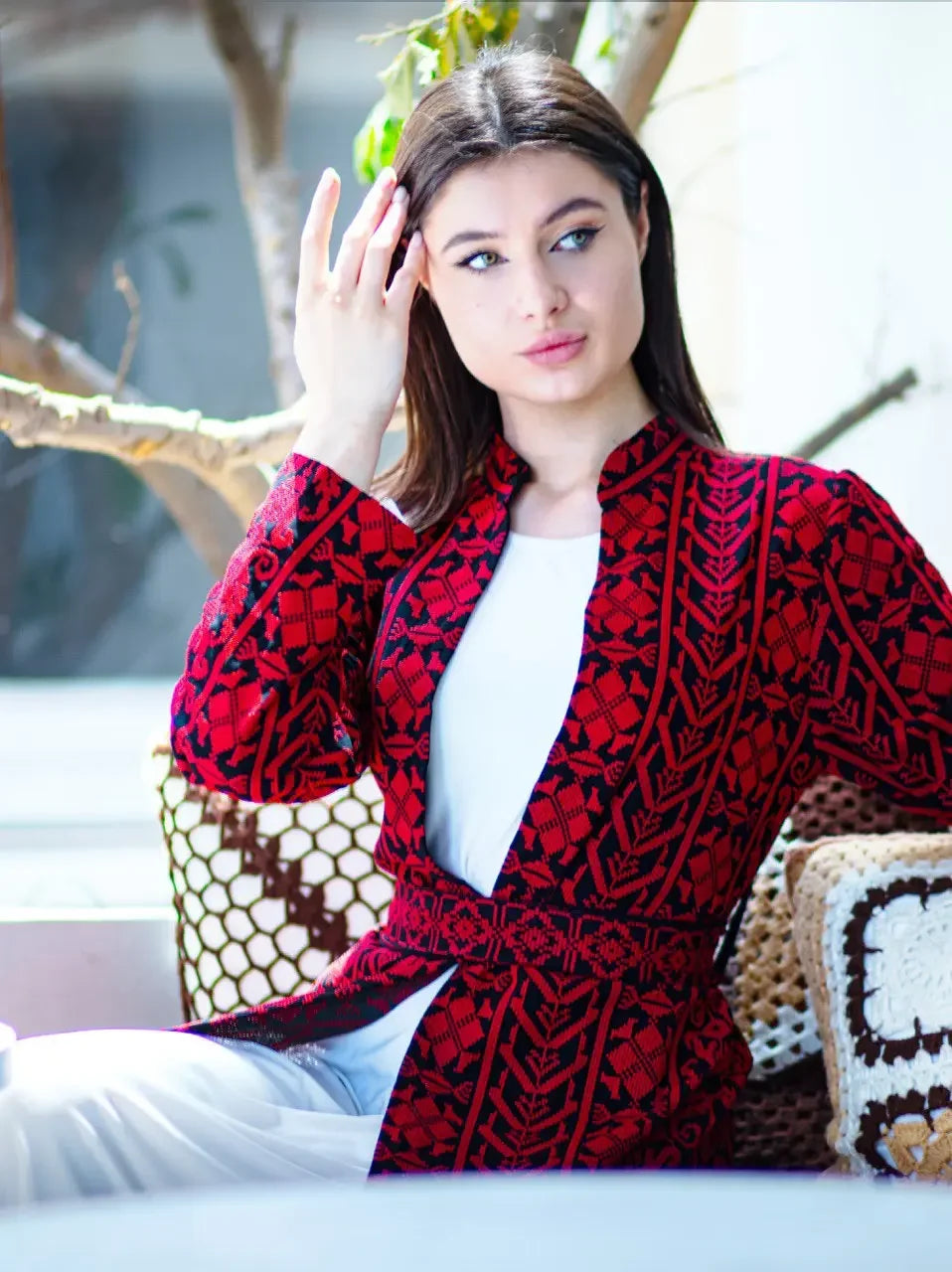 Woman wearing a red and black embroidered long cardigan from Palestinian Elegance sitting indoors