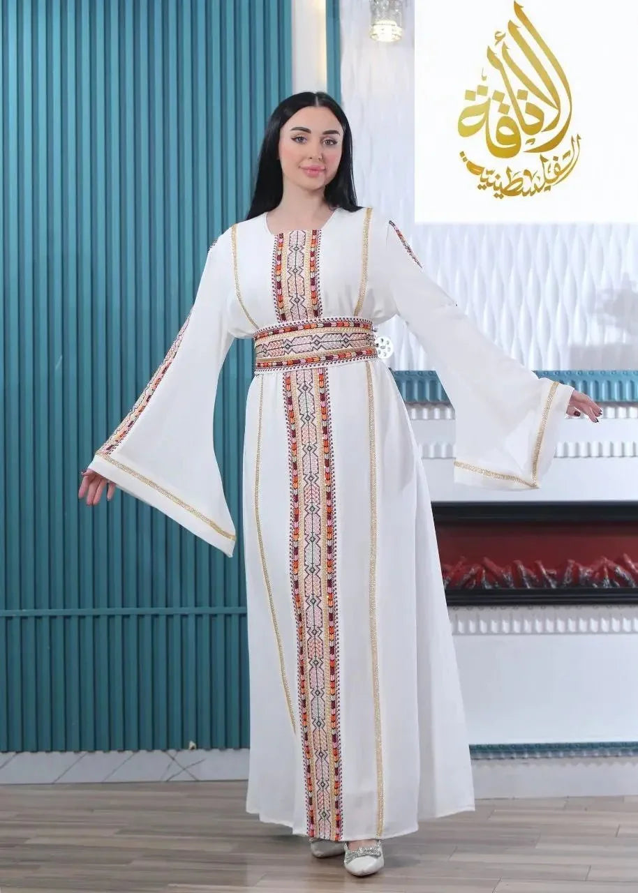 Woman wearing a white embroidered Palestinian kaftan with colorful traditional patterns and wide sleeves