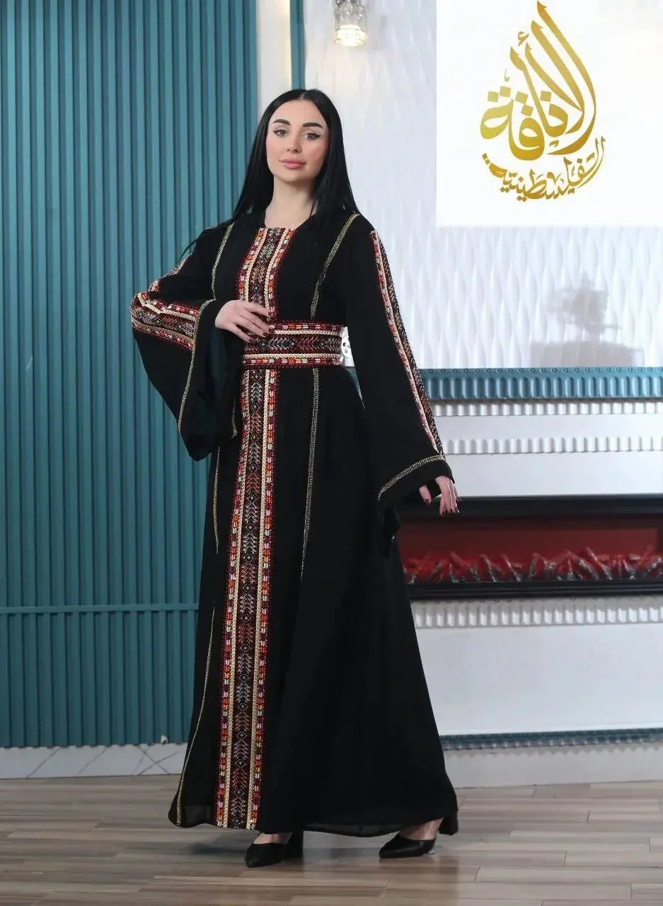 Woman wearing a black embroidered Palestinian kaftan with colorful traditional patterns and wide sleeves