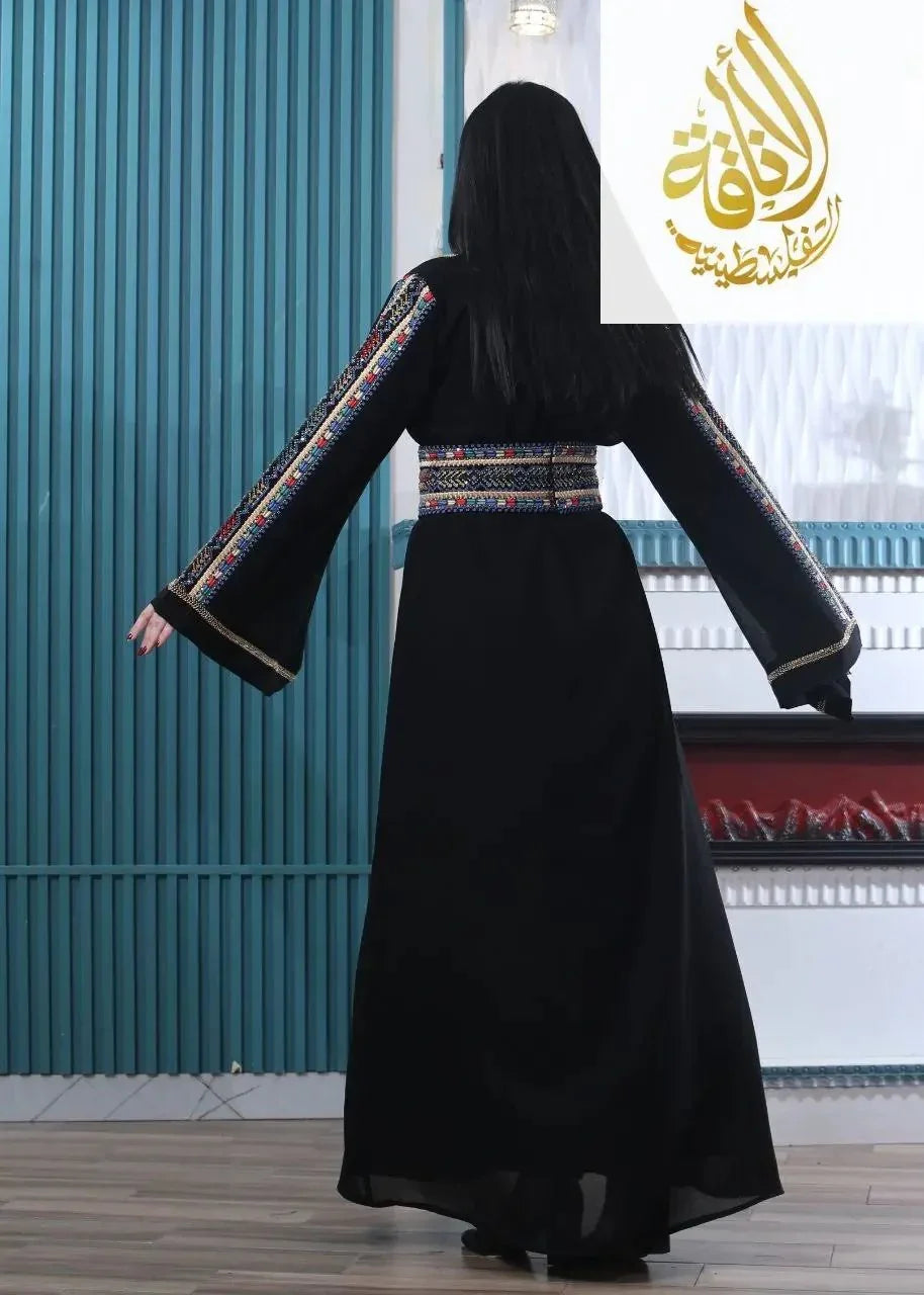 Woman wearing an embroidered Palestinian kaftan with colorful sleeve and waist details in a modern interior