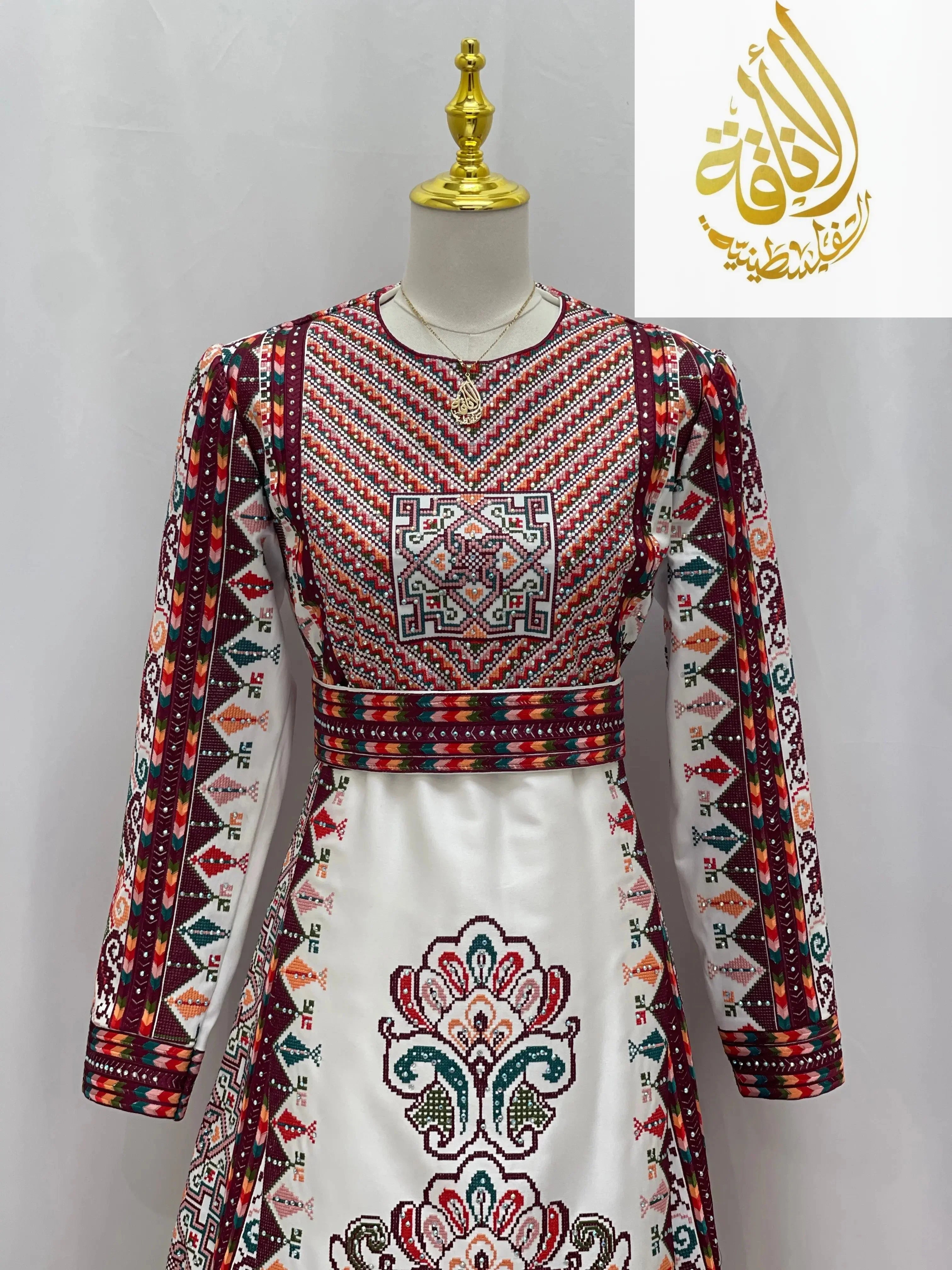 White Palestinian bridal thoub with intricate red and green embroidery and geometric patterns by Palestinian Elegance