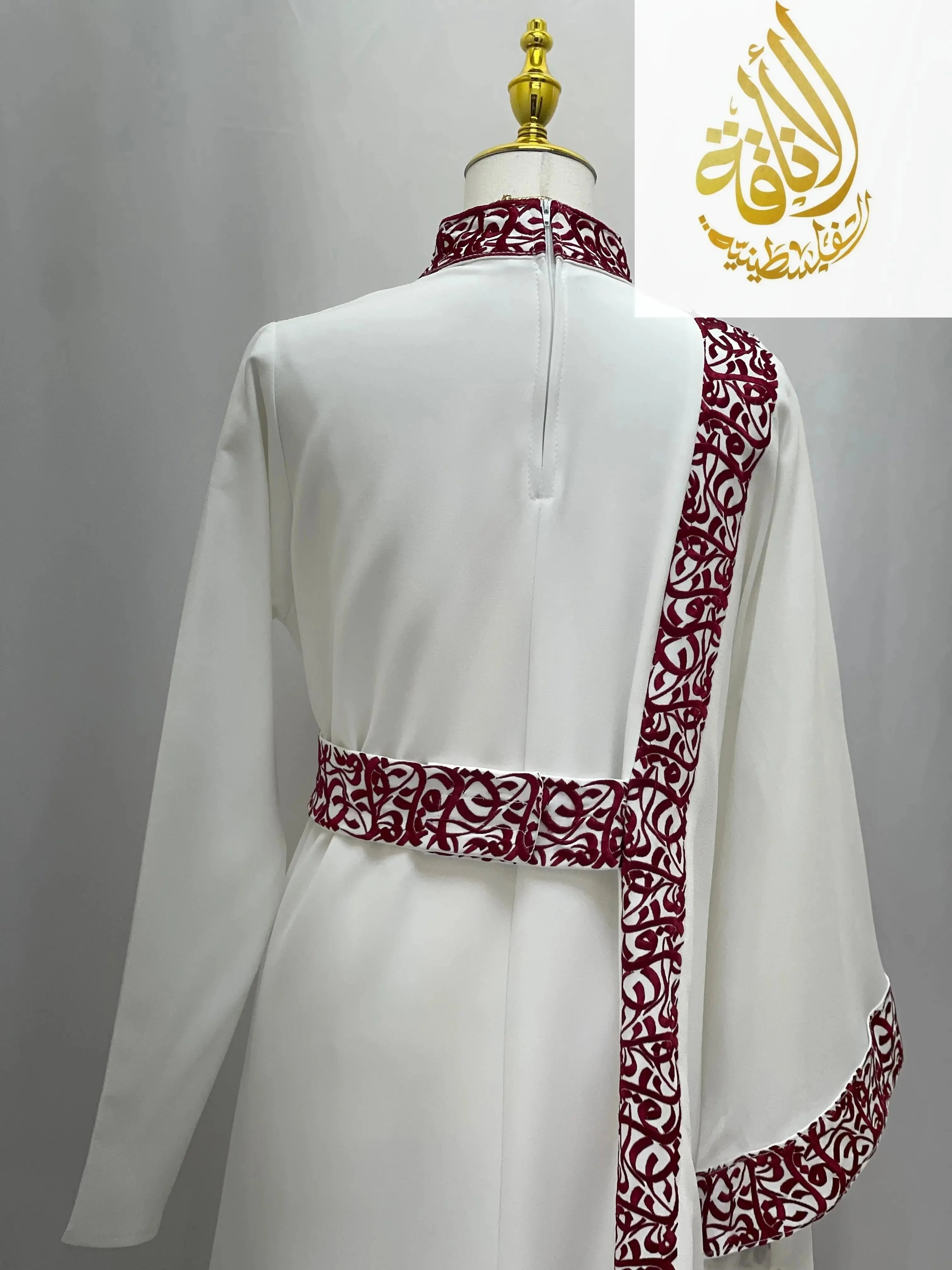 White embroidered abaya with Arabic letters detailing on collar, belt, and sleeve by Palestinian Elegance