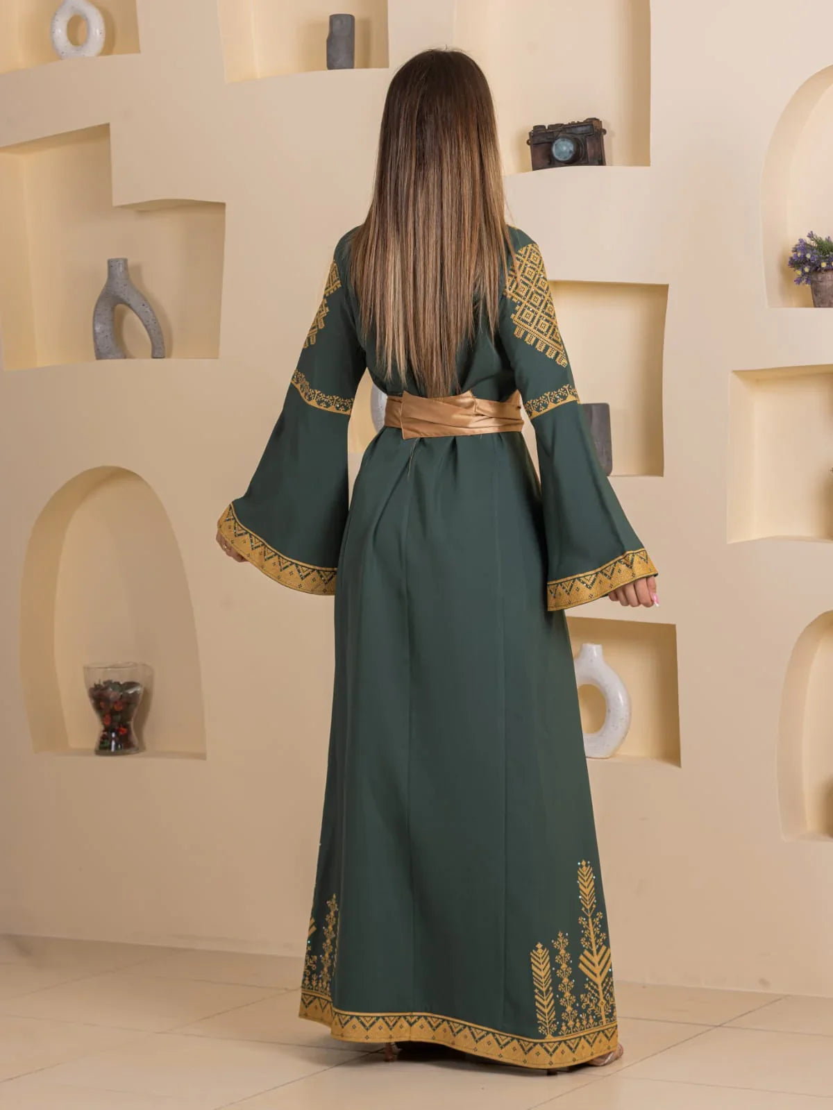 Back view of model in dark green Embroidered Elegance Dress with gold sash and intricate hem and sleeve embroidery