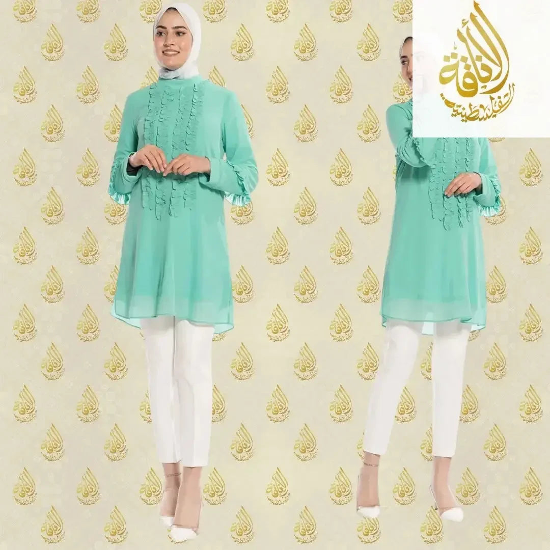 Luxury women's embroidered shirt in turquoise by Palestinian Elegance styled with white pants and heels