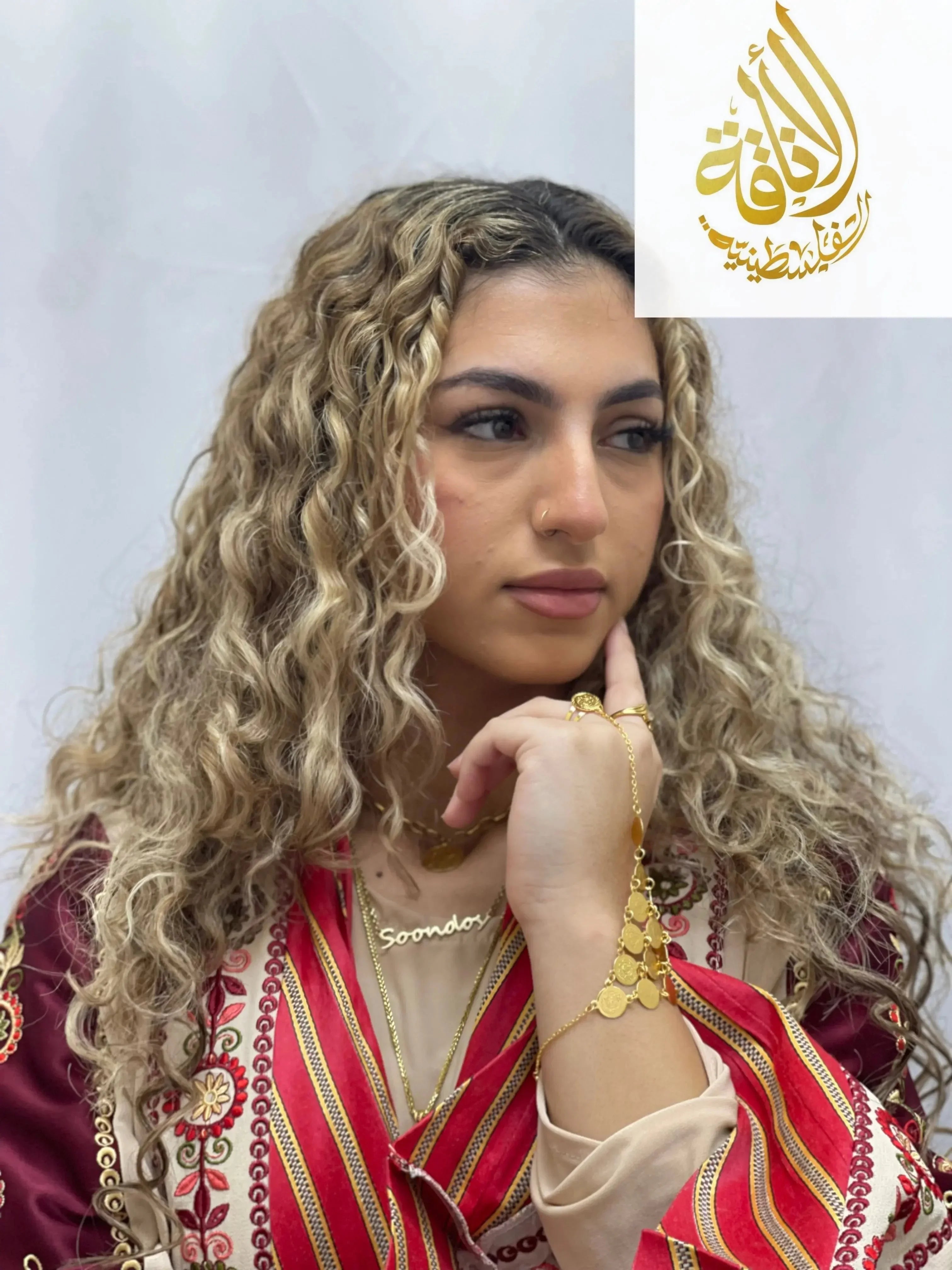 Woman wearing gold kaff hand jewelry and traditional Palestinian attire with curly blonde hair
