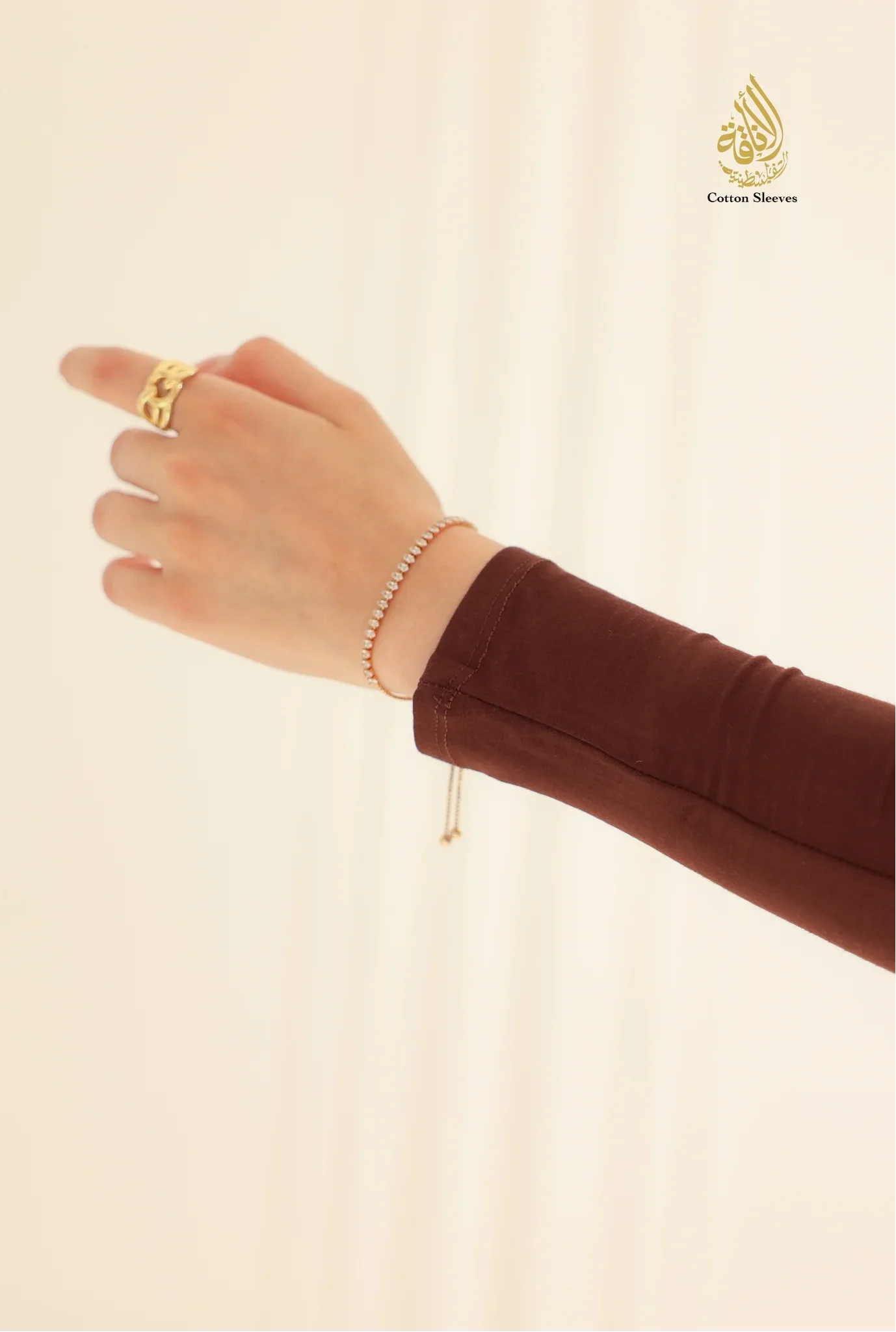 Hand wearing a gold ring and bracelet on a beige background