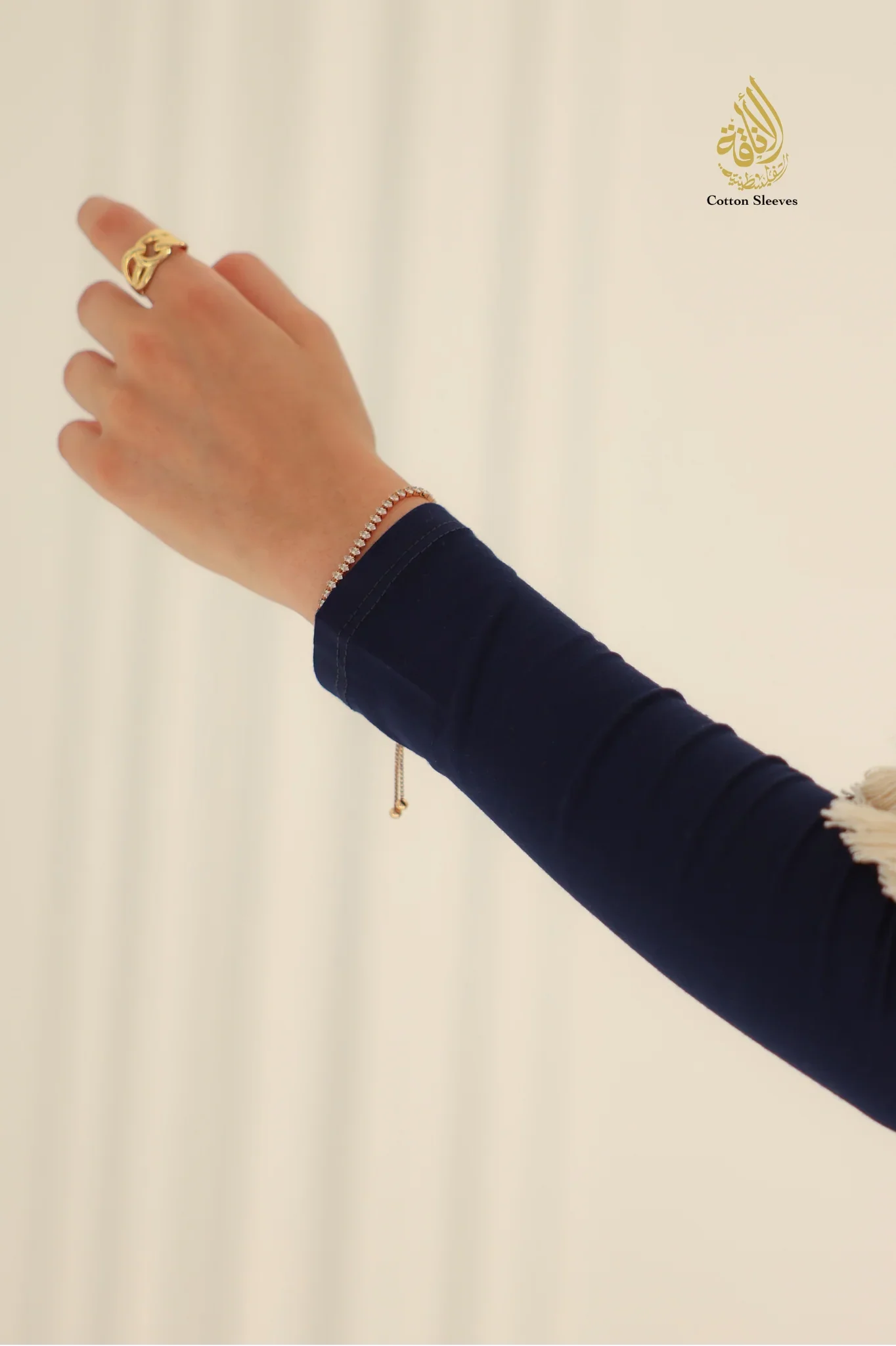 Hand wearing a gold ring and bracelet on a beige background