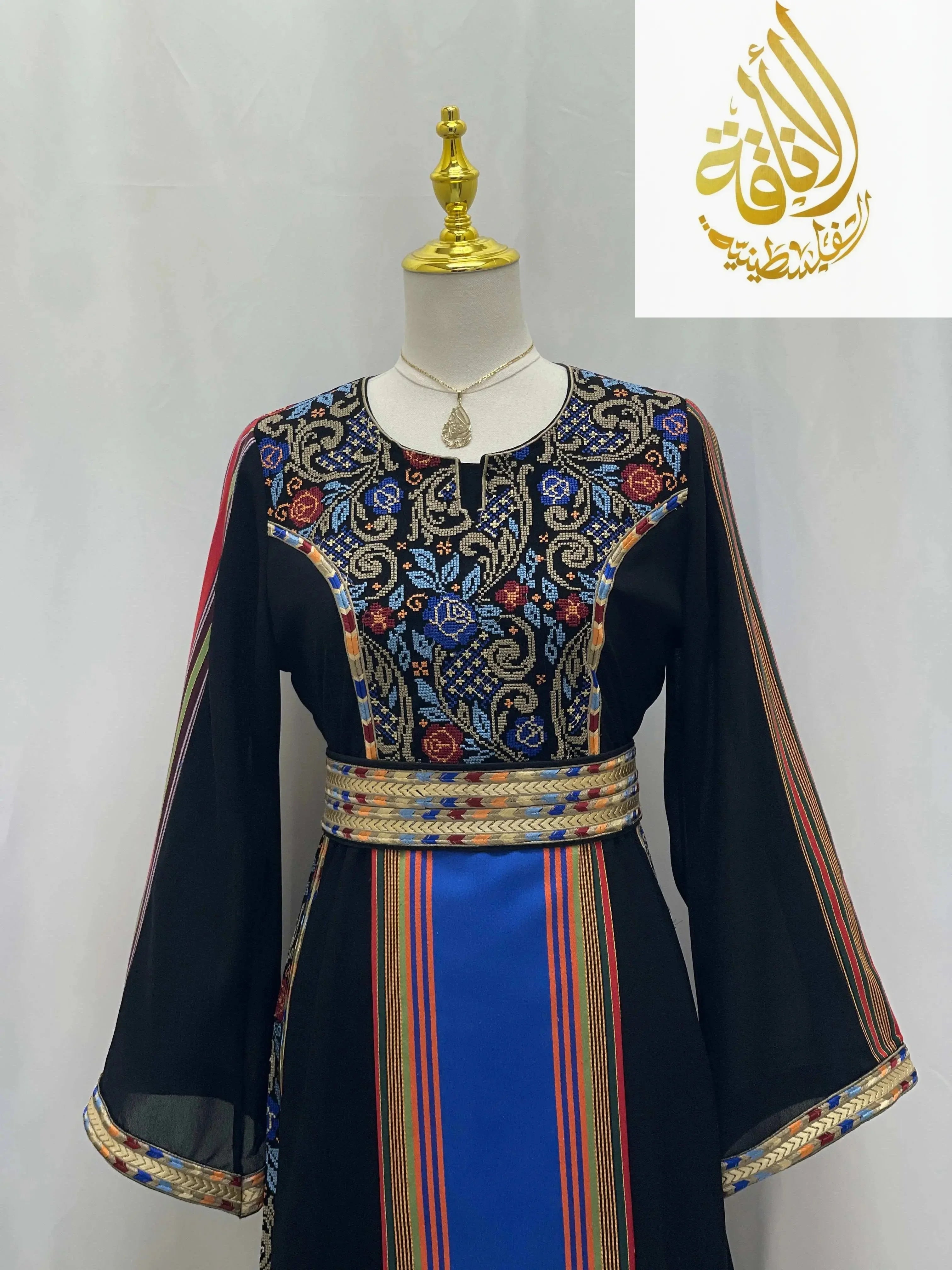 Haya Embroidered Majdalawe Dress by Palestinian Elegance with intricate floral embroidery and striped belt on black fabric