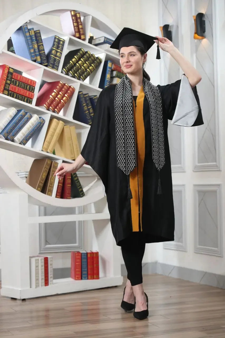 Graduate woman wearing Palestinian keffiyeh graduation stole with black gown and cap in library setting