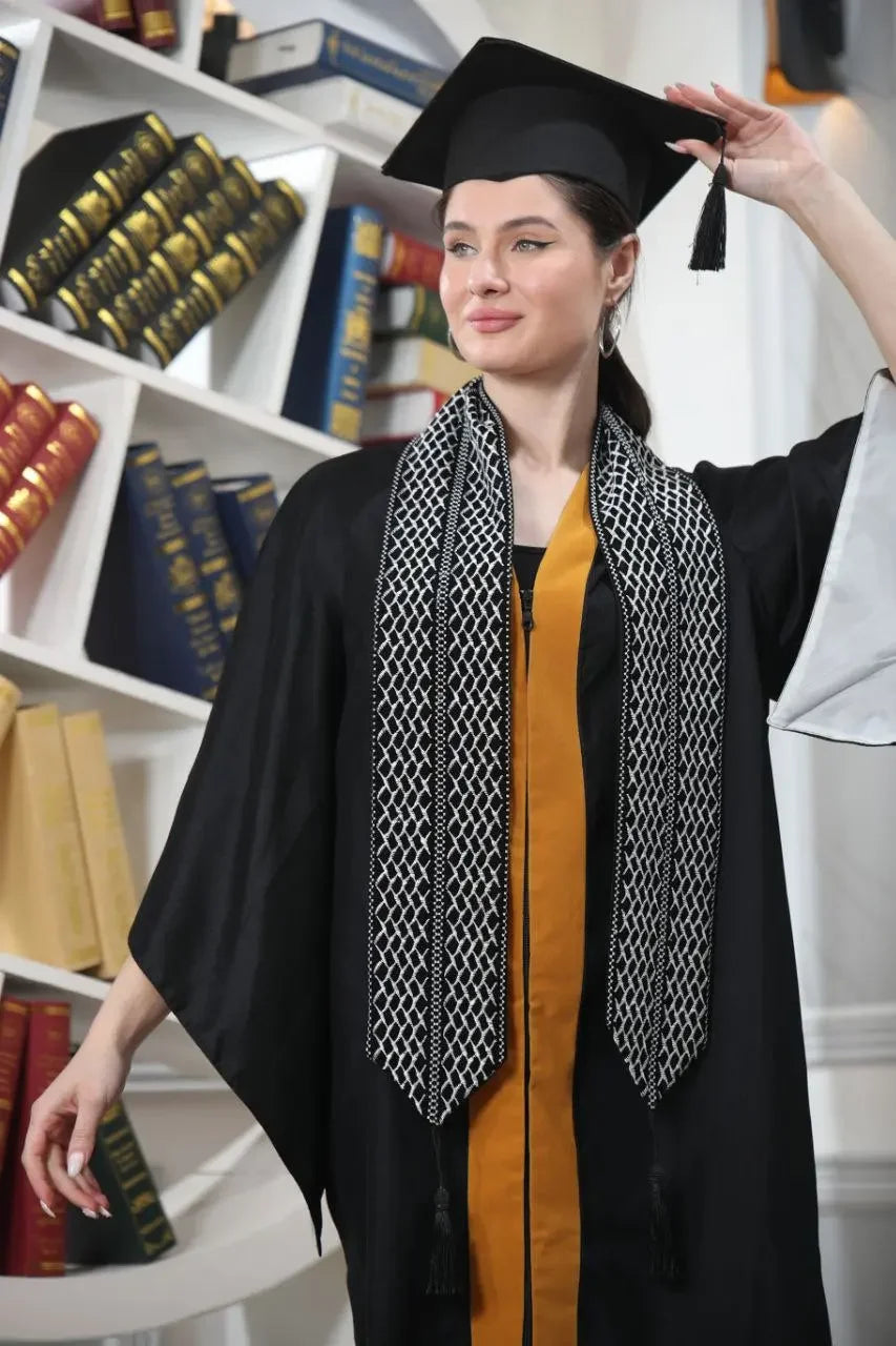 Graduate woman wearing Palestinian keffiyeh graduation stole over black and gold gown adjusting her cap