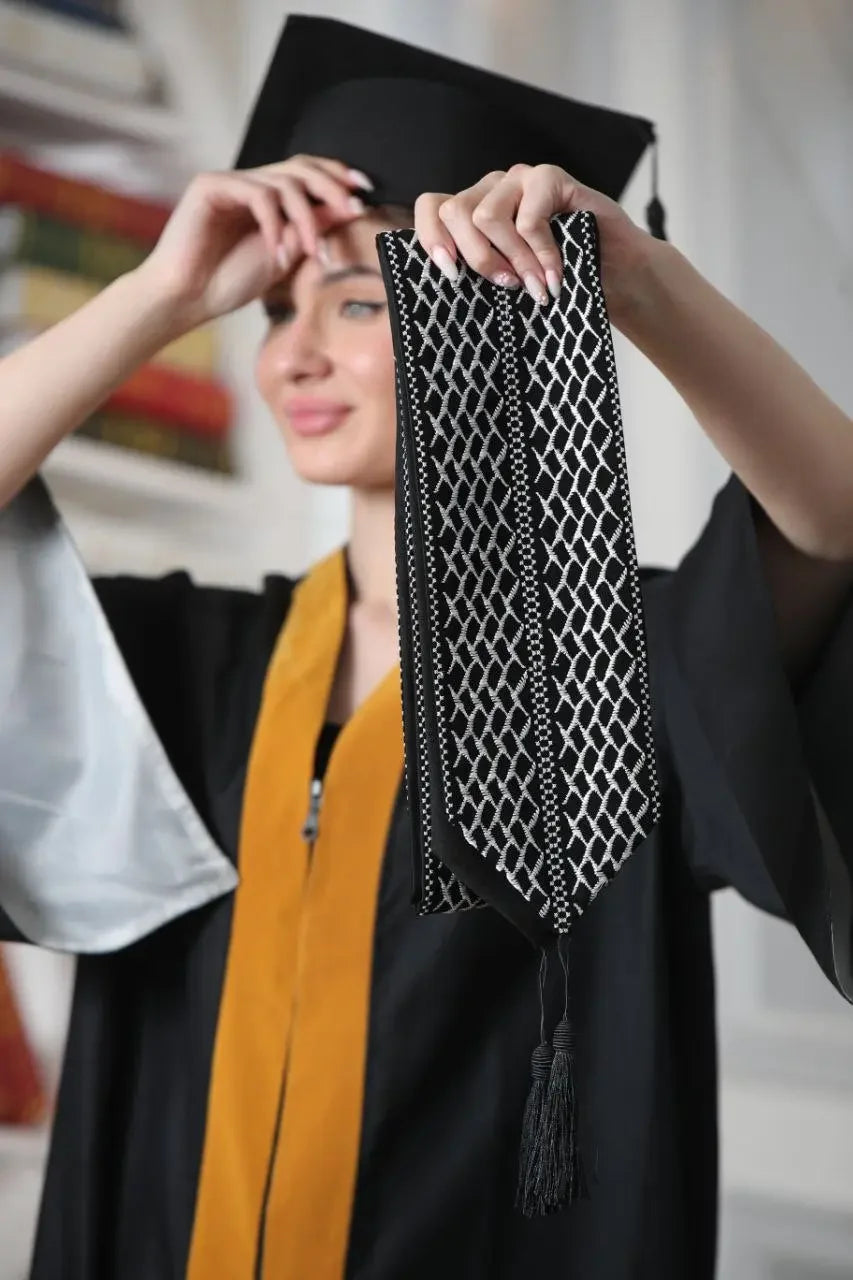 Palestinian keffiyeh graduation stole held by graduate wearing black cap and gown with gold sash