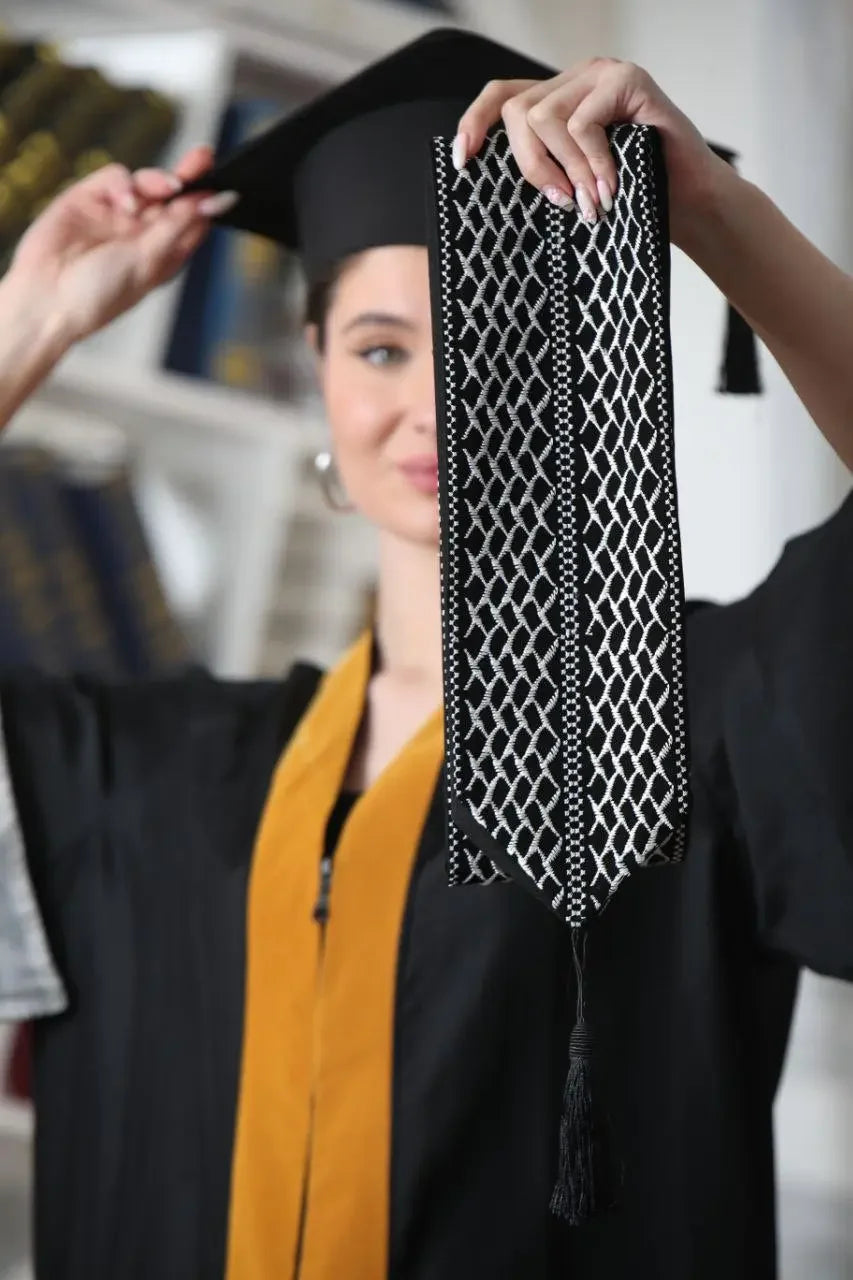 Palestinian keffiyeh graduation stole in black and white held by graduate in cap and gown