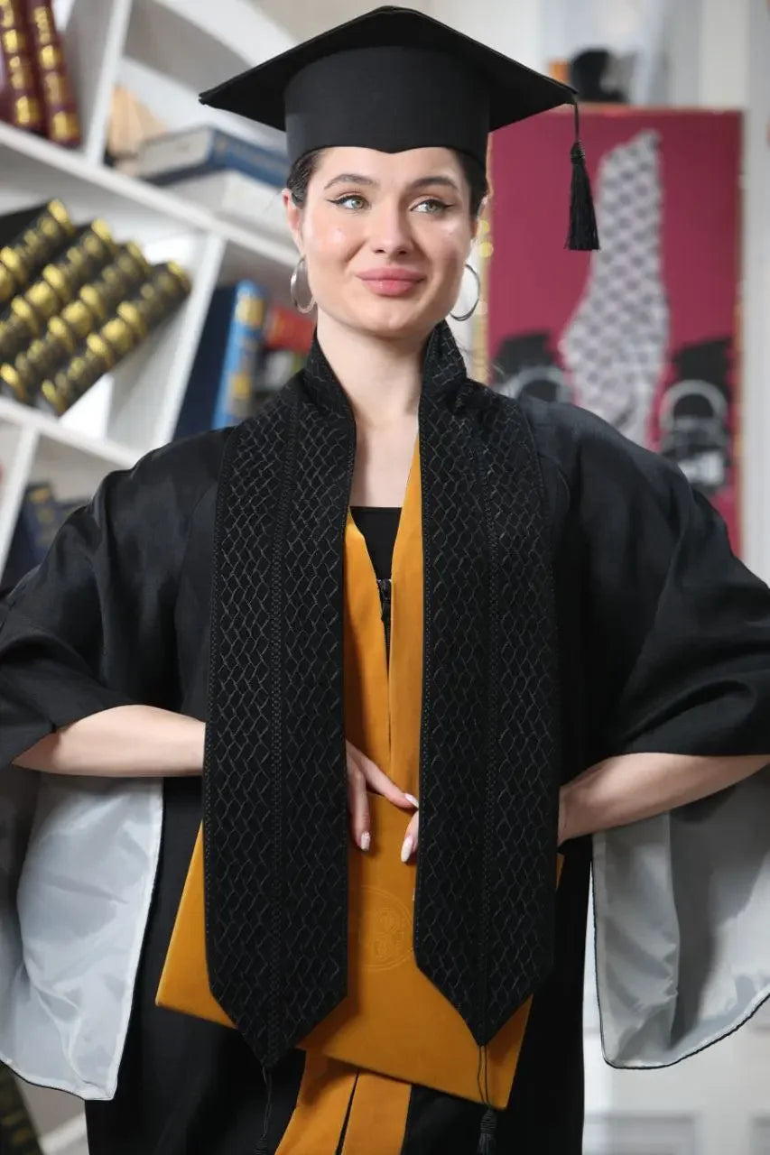 Graduate wearing Palestinian keffiyeh graduation stole and cap with black gown indoors