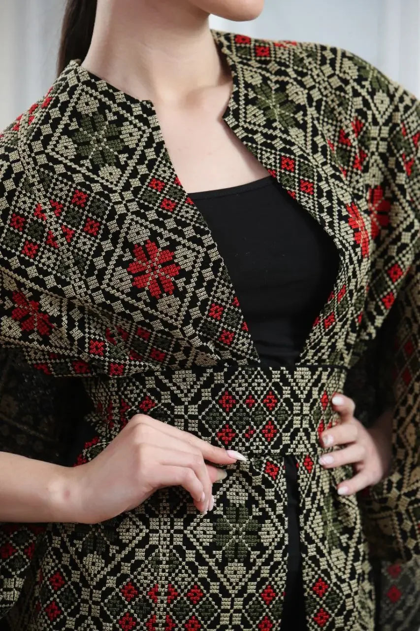 Palestinian tattreez cape with intricate red and green embroidery worn over black top by Palestinian Elegance