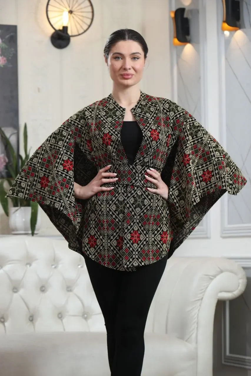 Palestinian tattreez cape with intricate red and black embroidery worn by model in modern living room