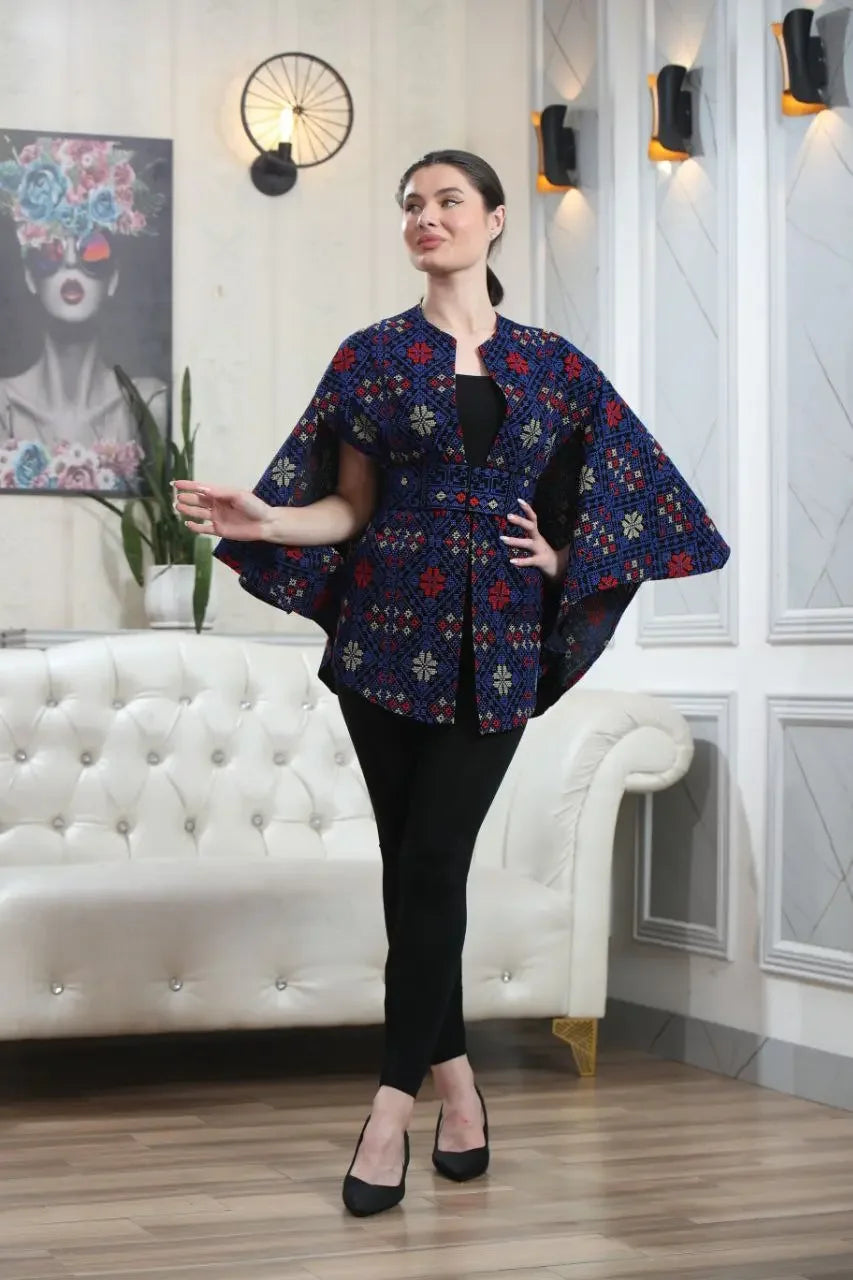 Woman wearing a Palestinian tattreez cape by Palestinian Elegance in a modern living room setting