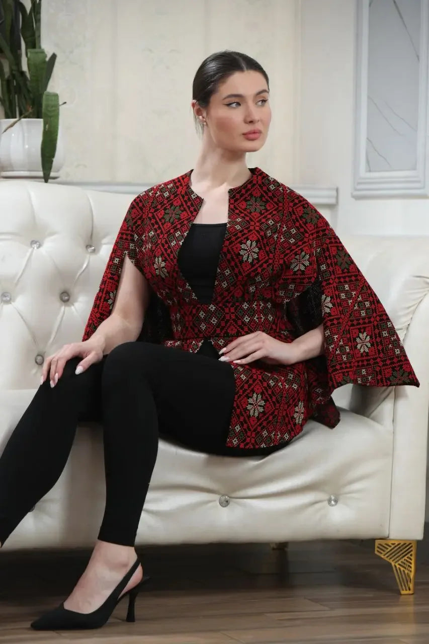 Woman wearing a Palestinian tattreez cape in red and black sitting on white sofa casual style