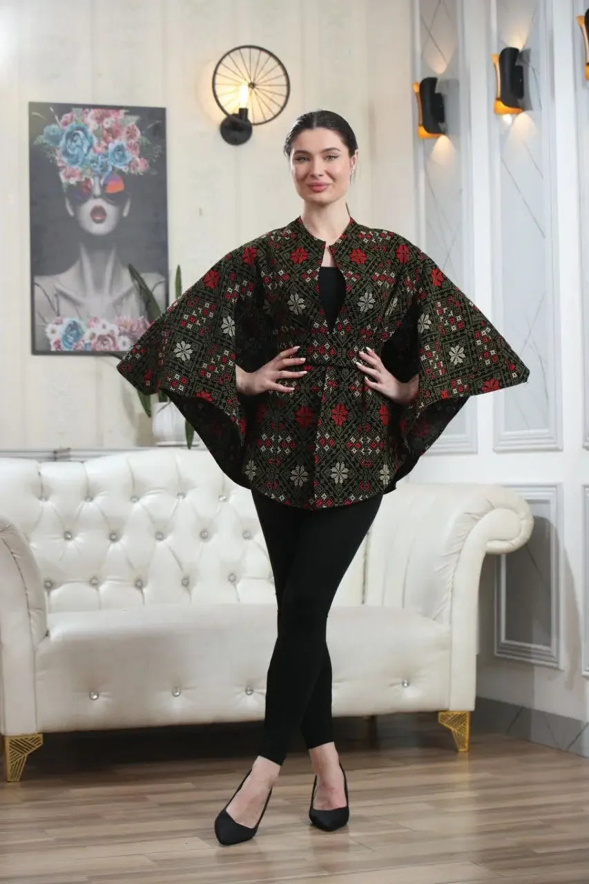 Woman wearing a casual Palestinian tattreez cape with traditional embroidery standing in a stylish living room