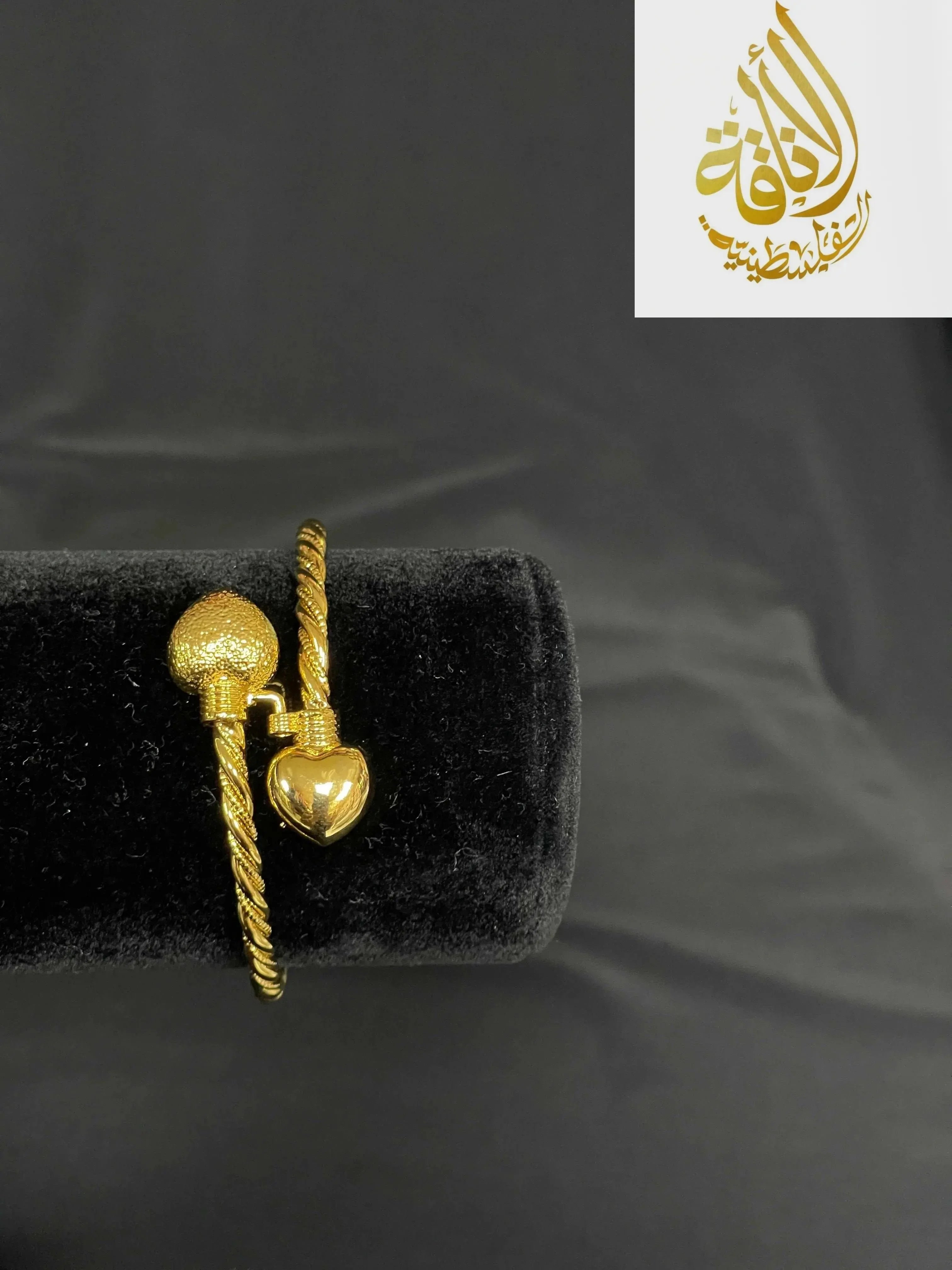 Palestinian Elegance Mabroma Gold Heart Bracelet with twisted band and heart-shaped charms on black display