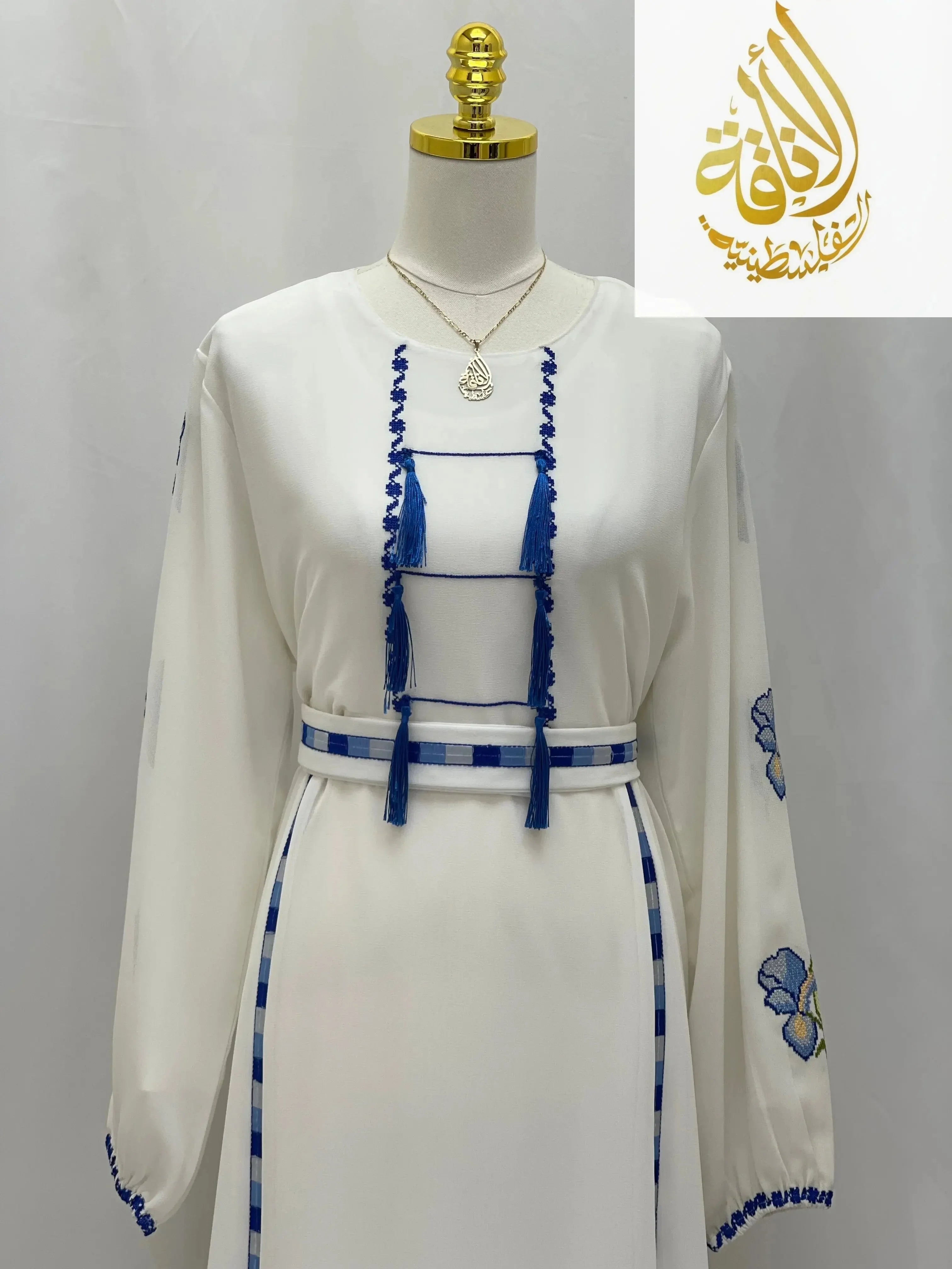 Palestinian embroidered dress in white with blue embroidery and tassel details by Palestinian Elegance
