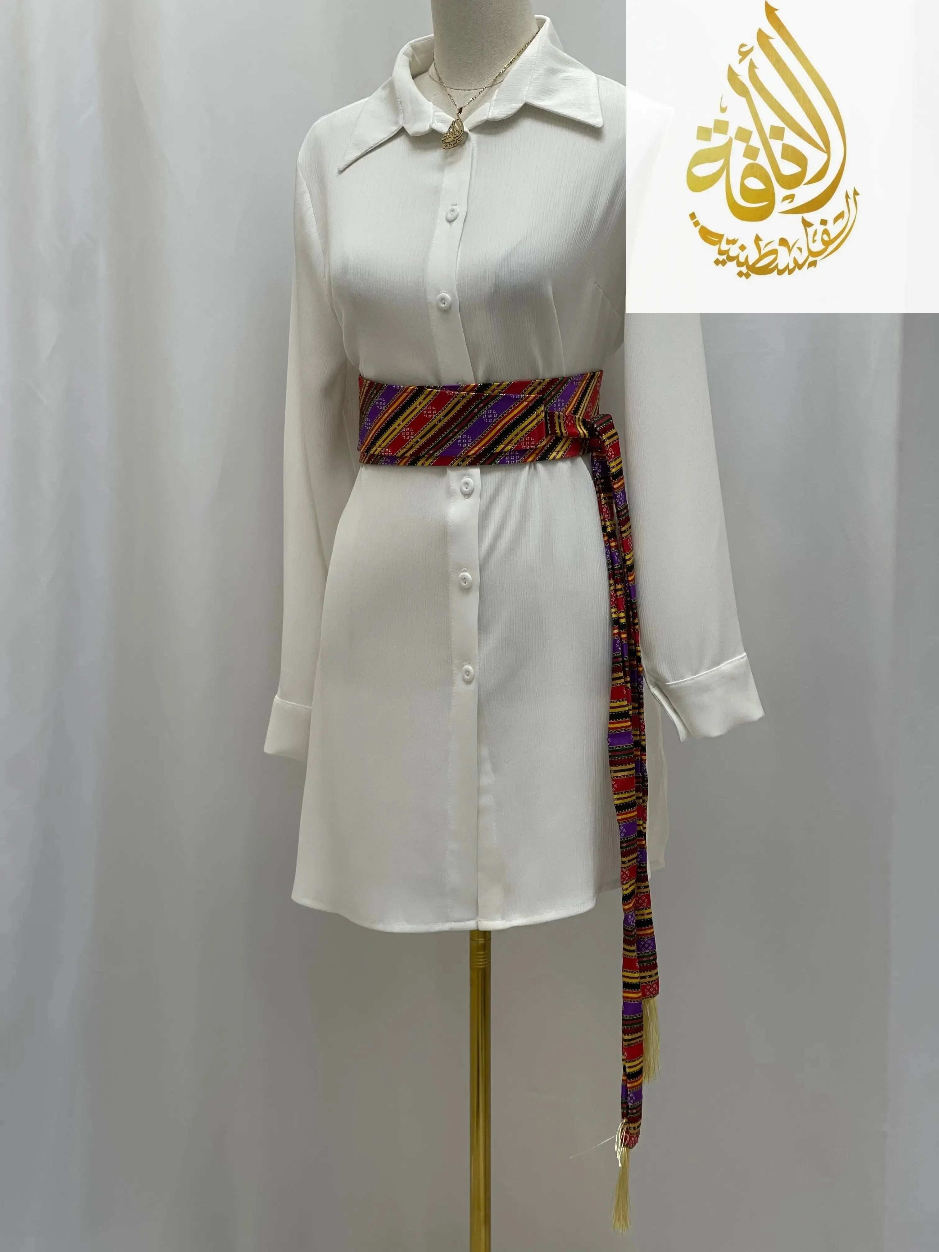 Palestinian embroidered belt wrapped around a white button-up dress on a mannequin