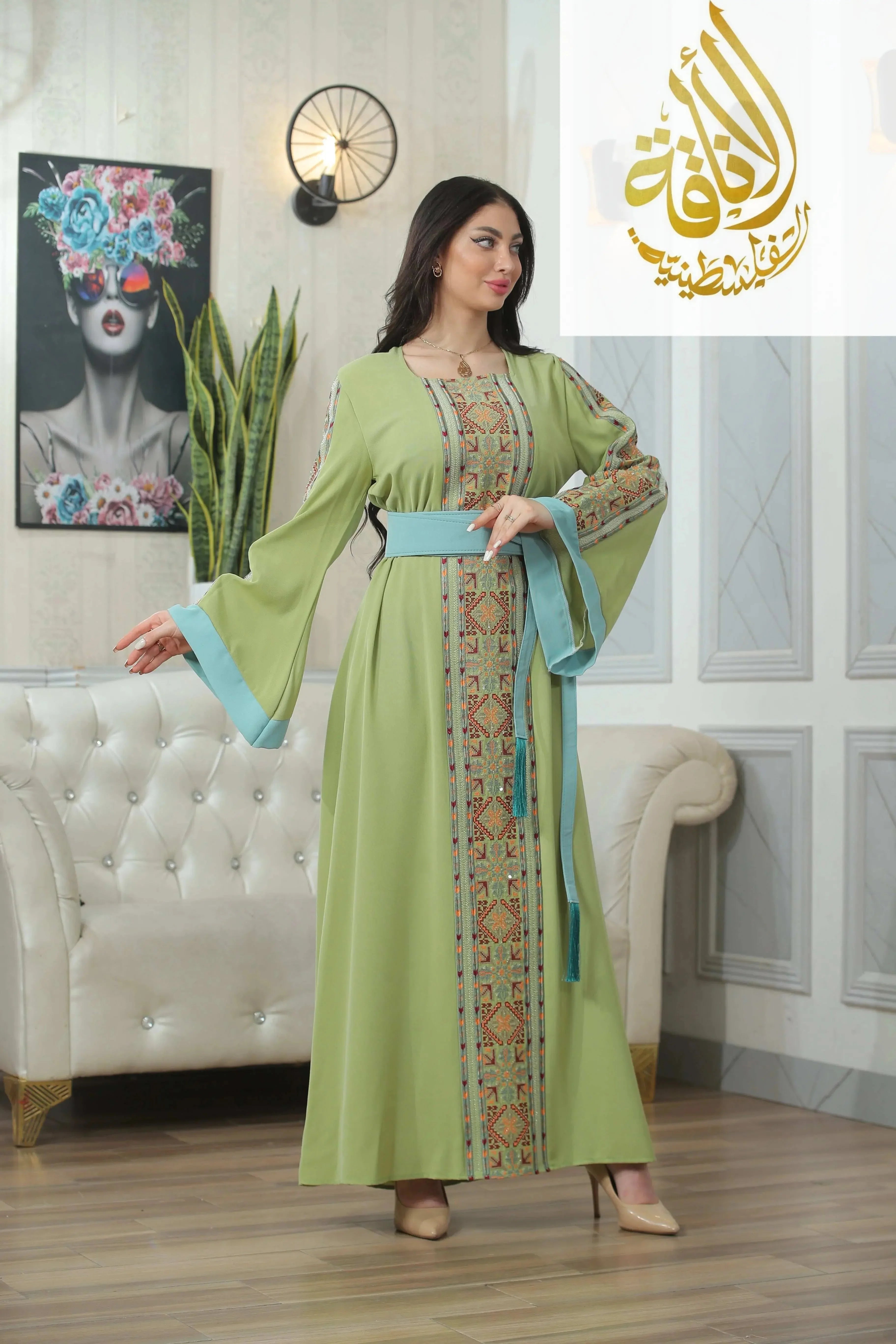 Palestinian Elegance green Nadera Embroidered Thoub with intricate embroidery and blue belt worn by model indoors