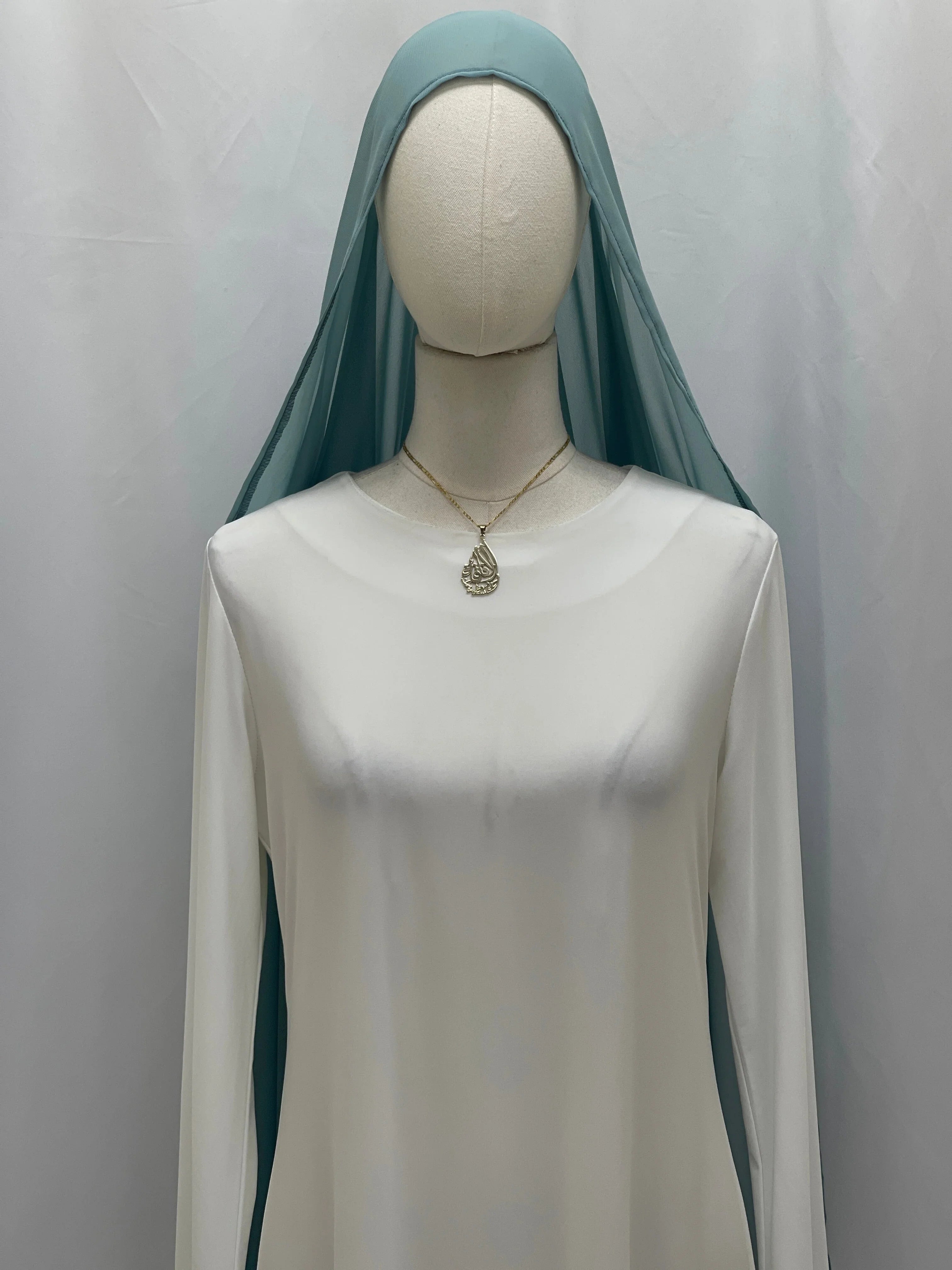 Palestinian Elegance mannequin wearing New Khirka With White tassel teal draped over white dress and gold pendant