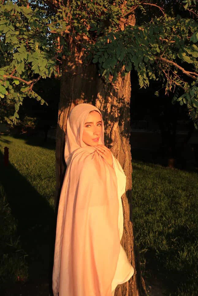 Palestinian Elegance New Modal Hijab light pink draped on model leaning against tree in sunset park