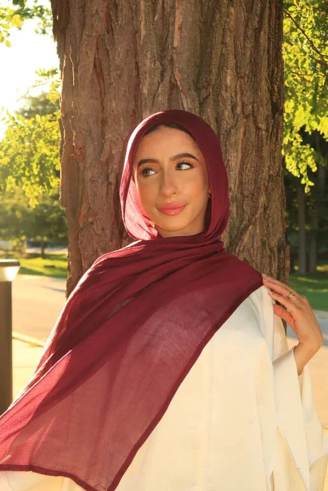New Modal Hijab burgundy draped on woman leaning against tree outdoors by Palestinian Elegance