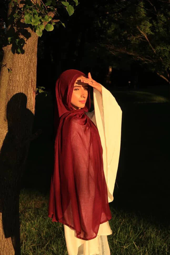 Palestinian Elegance model wearing a maroon New Modal Hijab draped over white dress in golden sunlight