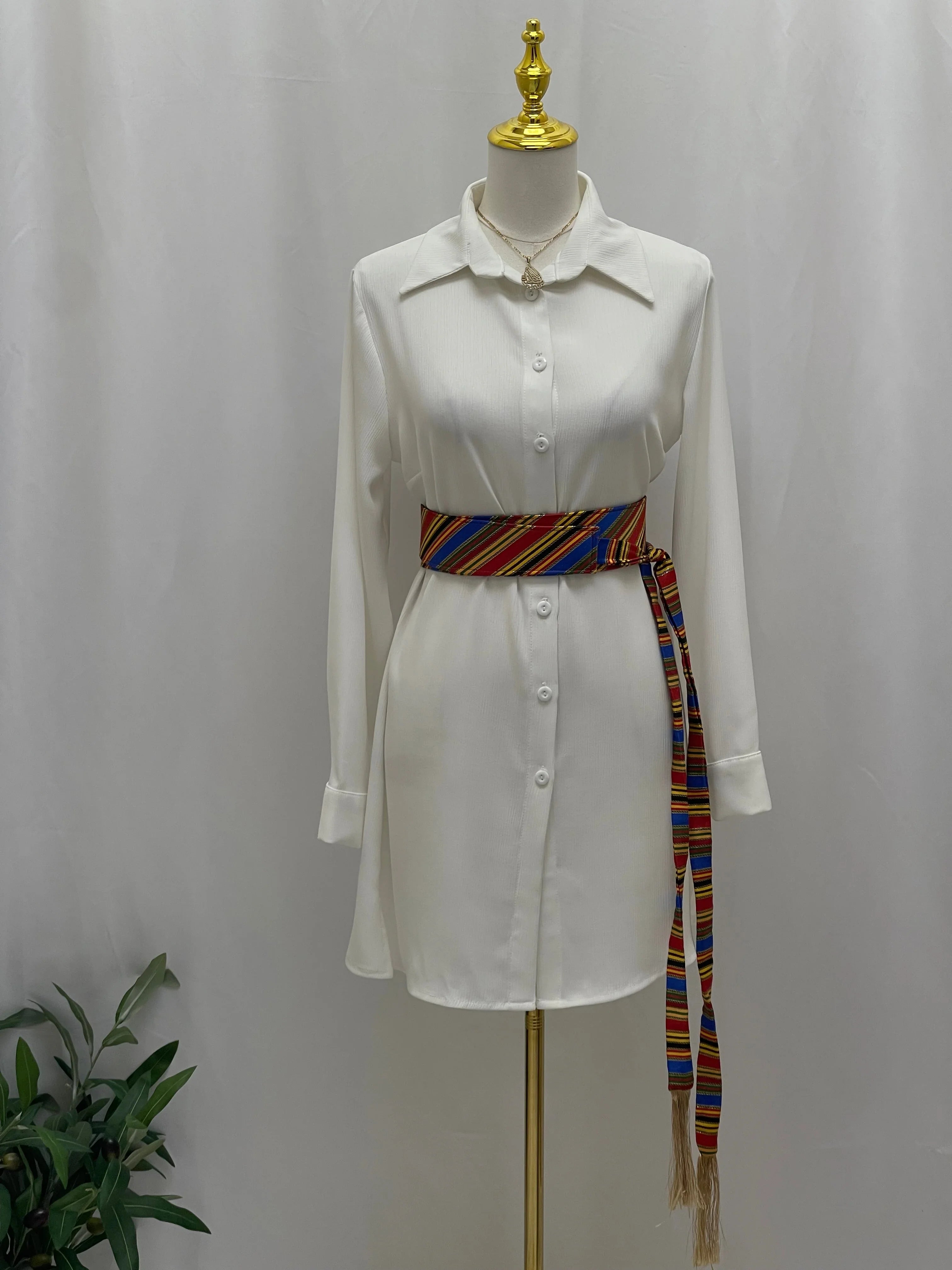White button down shirt dress on mannequin styled with Palestinian Elegance Saya Belt colorful woven waist sash with tassels