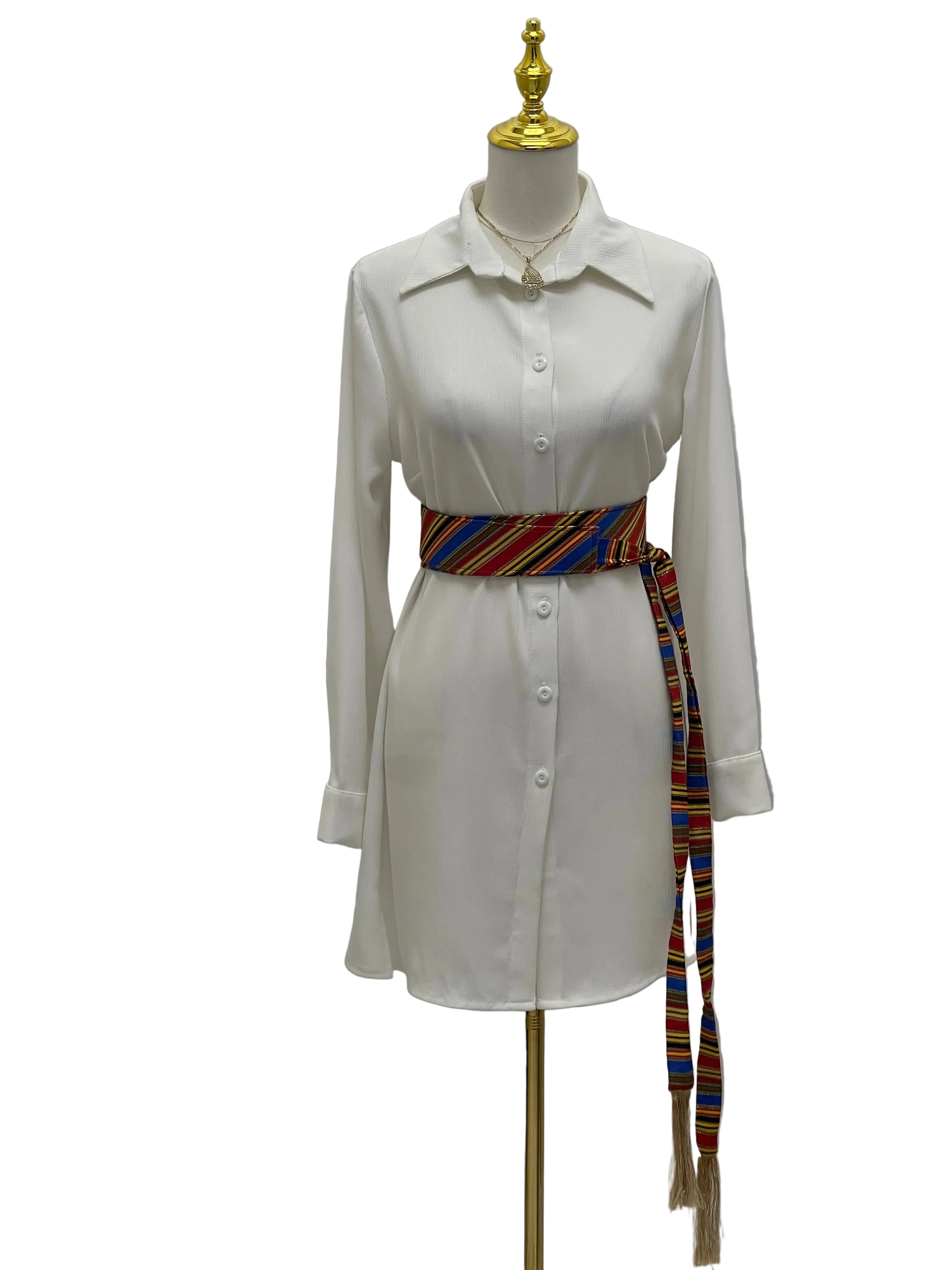 White button down shirt dress on mannequin styled with Palestinian Elegance Saya Belt colorful woven waist sash with tassels