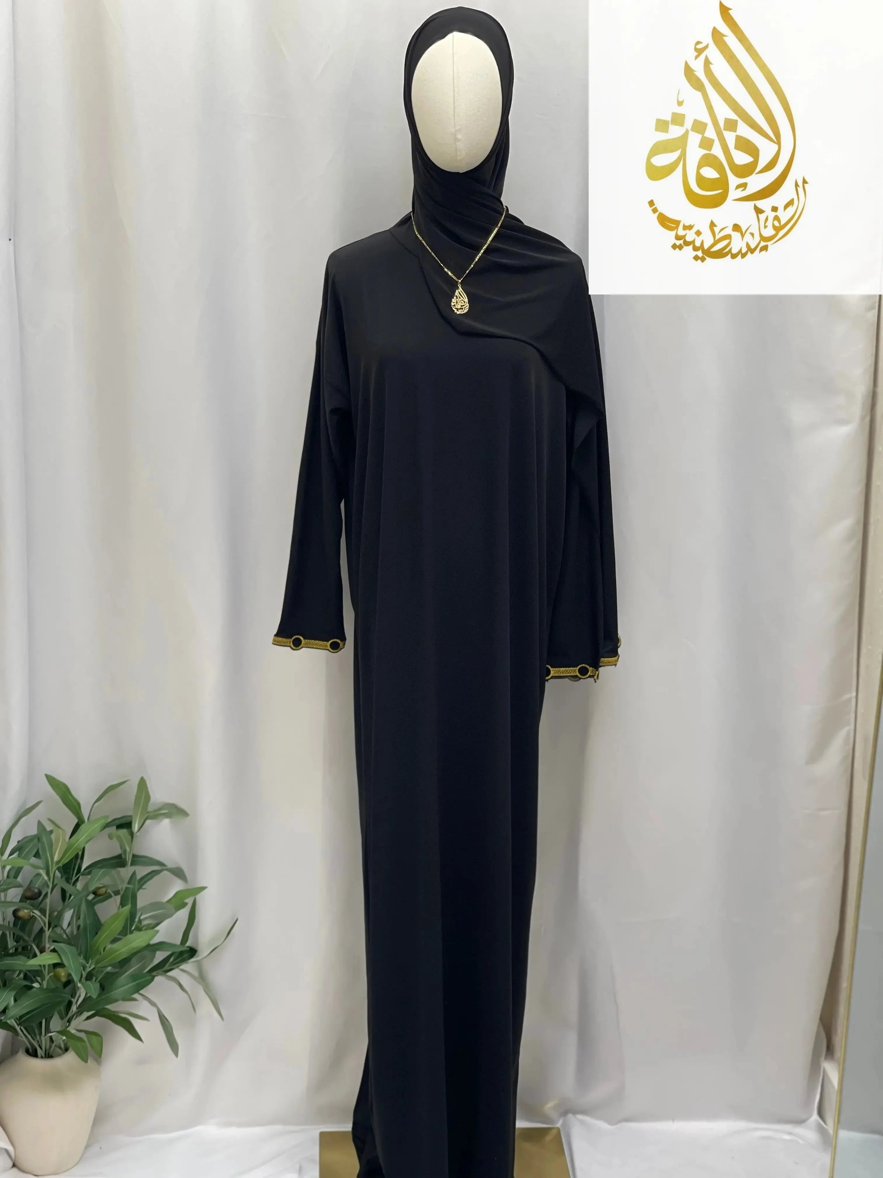 Black comfortable one piece prayer dress with long sleeves and gold trim on cuffs displayed on mannequin