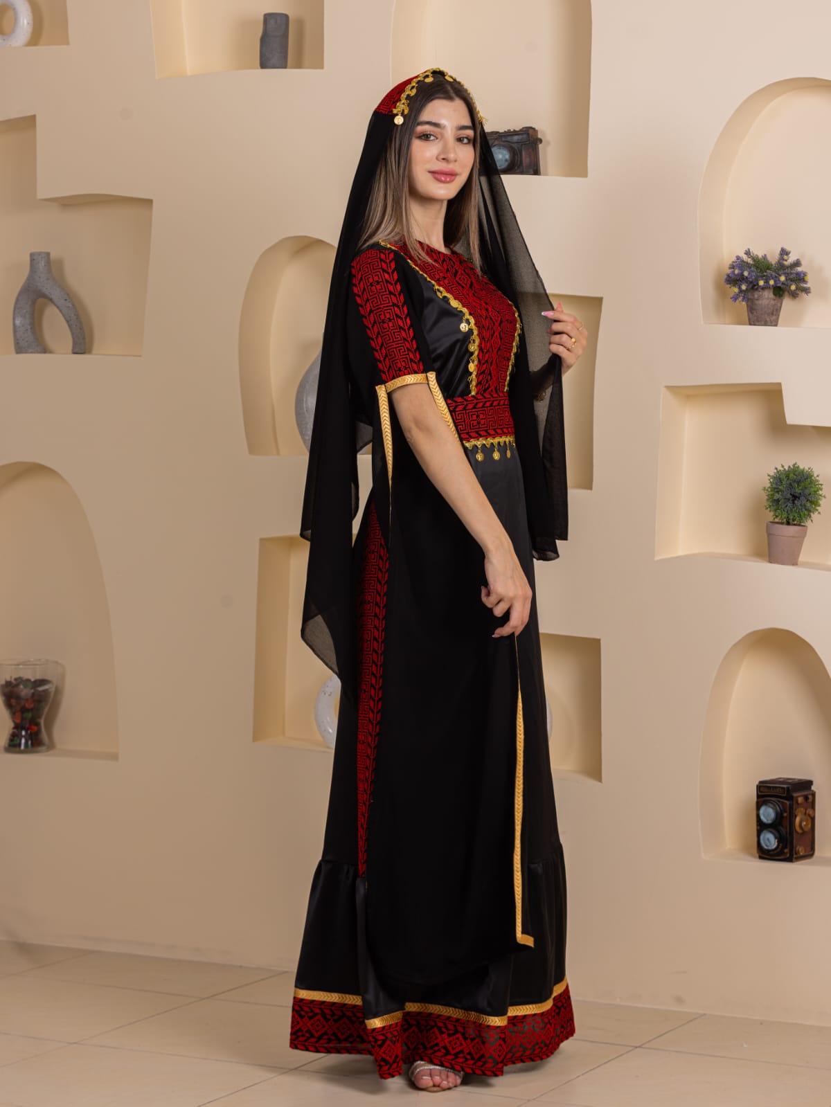 Model wearing Qamar Embroidered Dress by Palestinian Elegance black maxi dress with red embroidery gold trim and veil