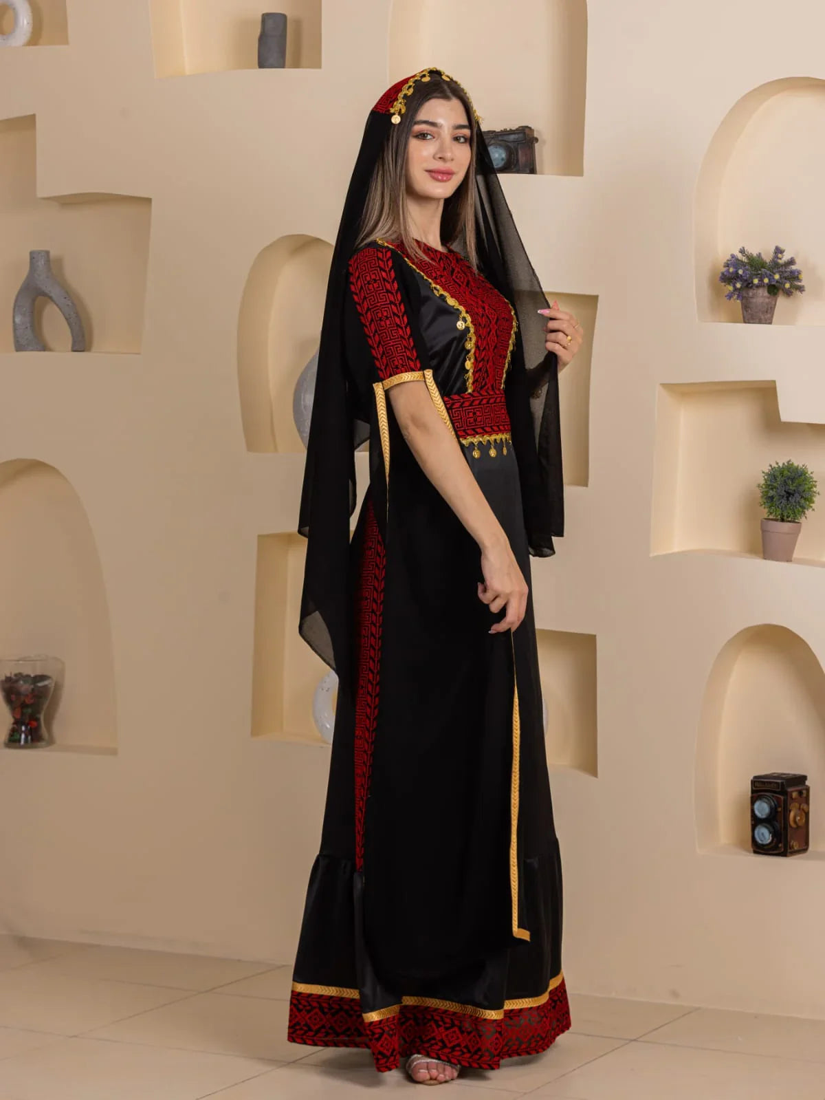 Model wearing Qamar Embroidered Dress by Palestinian Elegance black maxi dress with red embroidery gold trim and veil